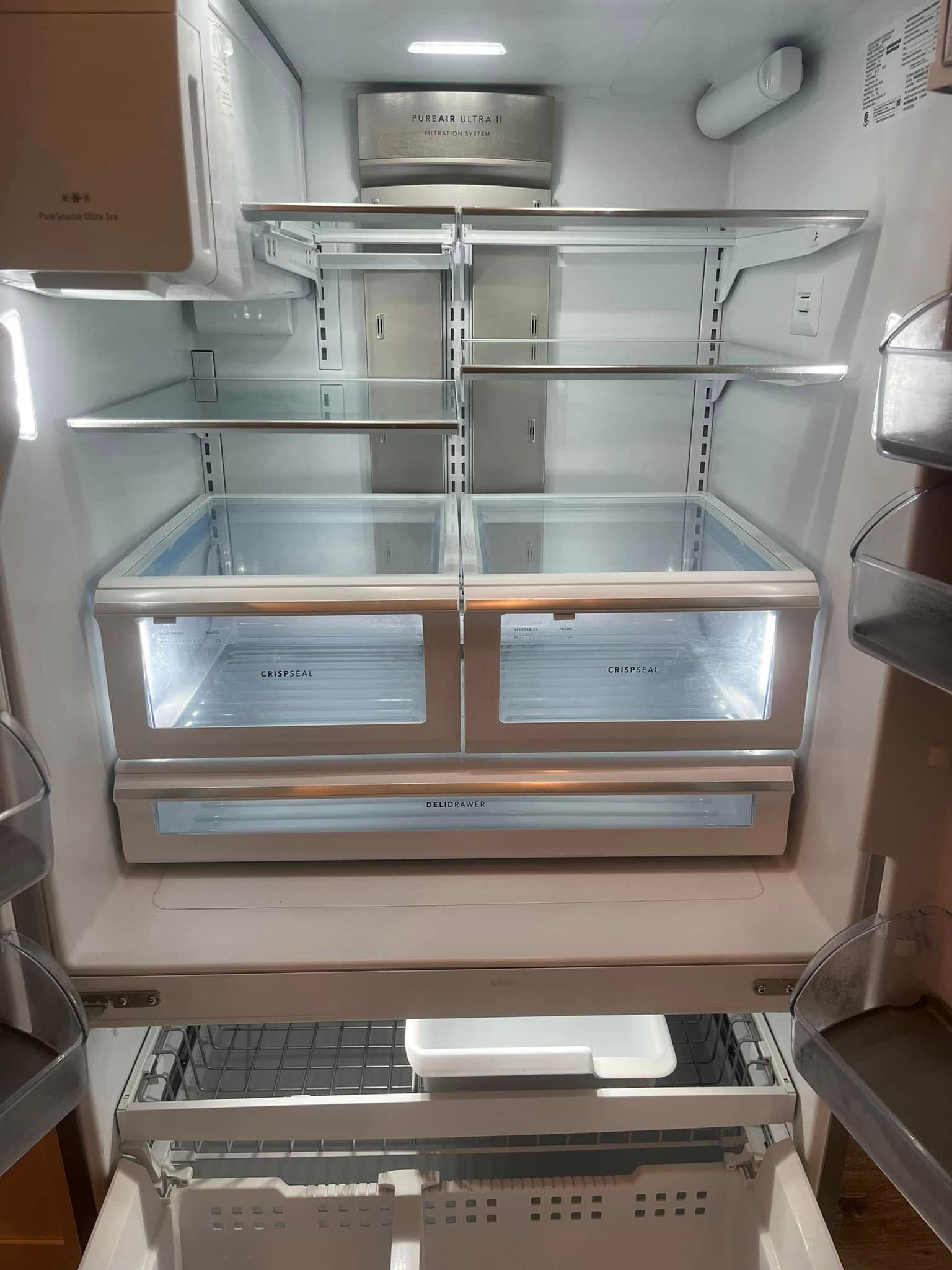 Empty refrigerator interior with multiple shelves and drawers, illuminated with bright white light.