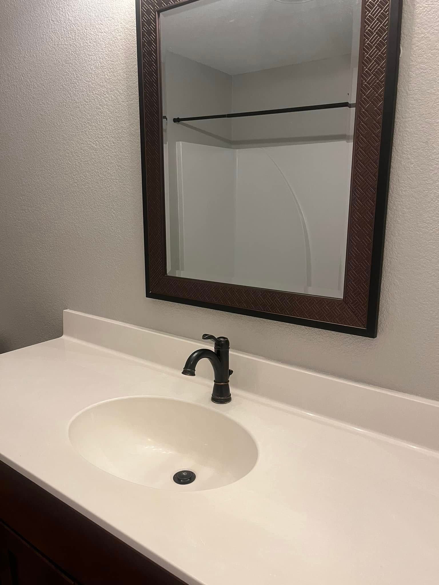 Bathroom vanity with white countertop, oval sink, dark faucet, and decorative mirror.