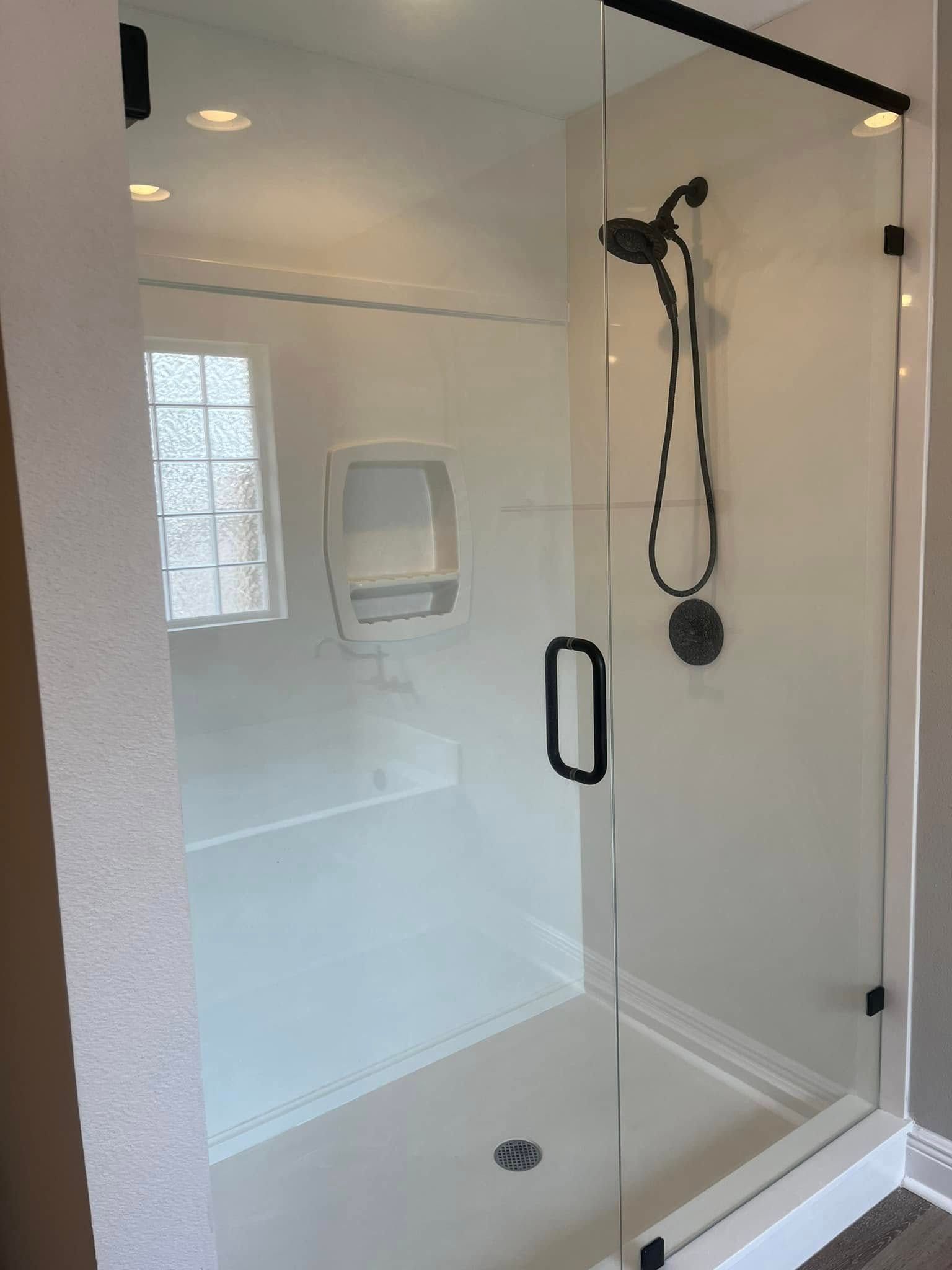Glass shower enclosure with black fixtures and white walls.