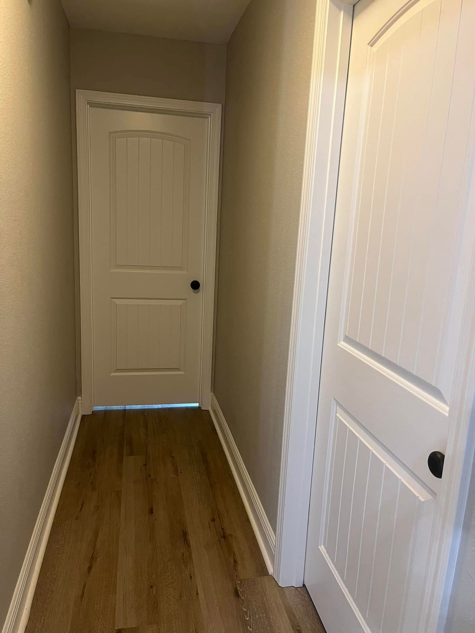 Narrow hallway with two white doors and wood-look flooring.