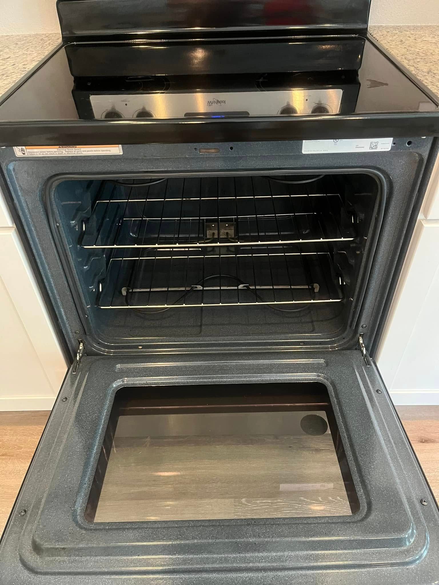 Black oven door open, revealing empty interior with racks and light. Stainless steel cooktop visible above.