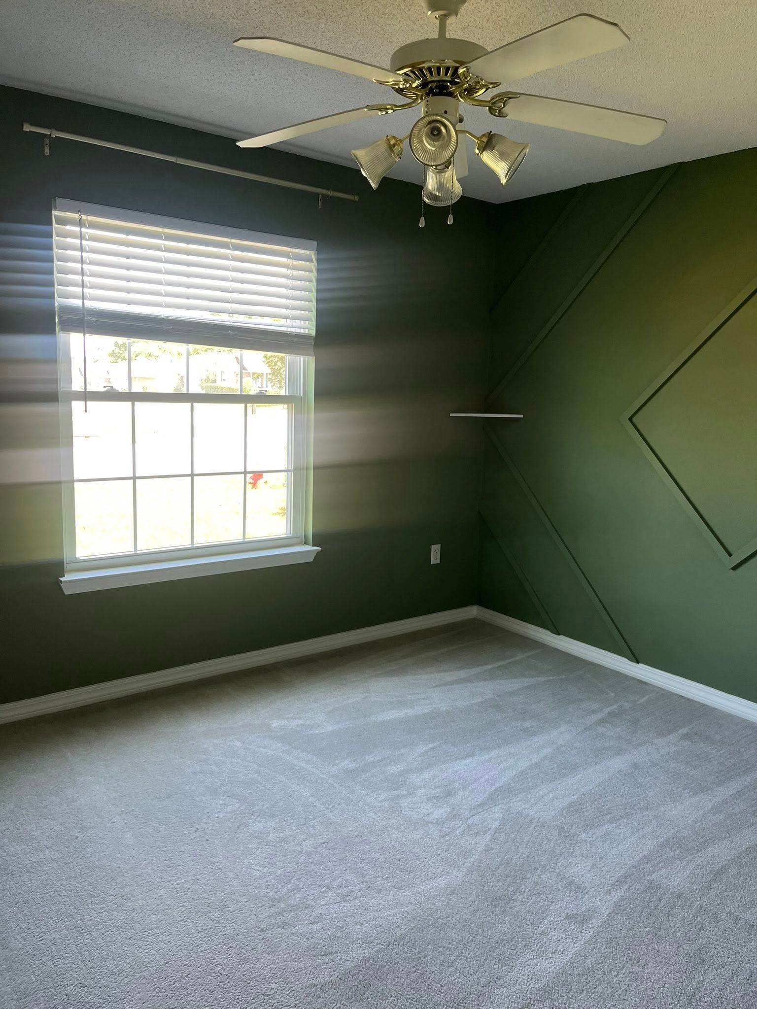 Empty room with green walls, diamond accents, window with blinds, and ceiling fan. Gray carpet.