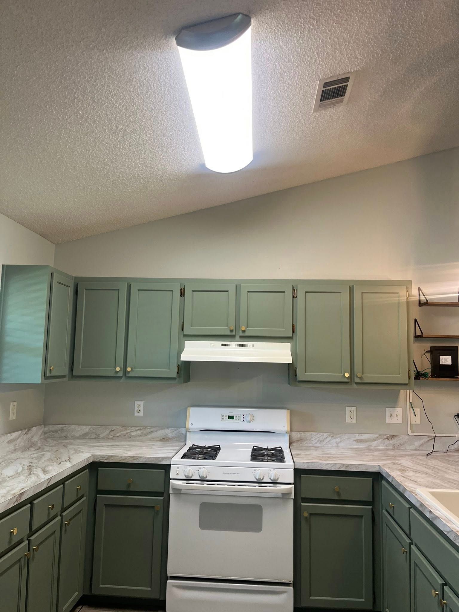 Green kitchen cabinets and white appliances in a kitchen with a white stove and overhead lighting.