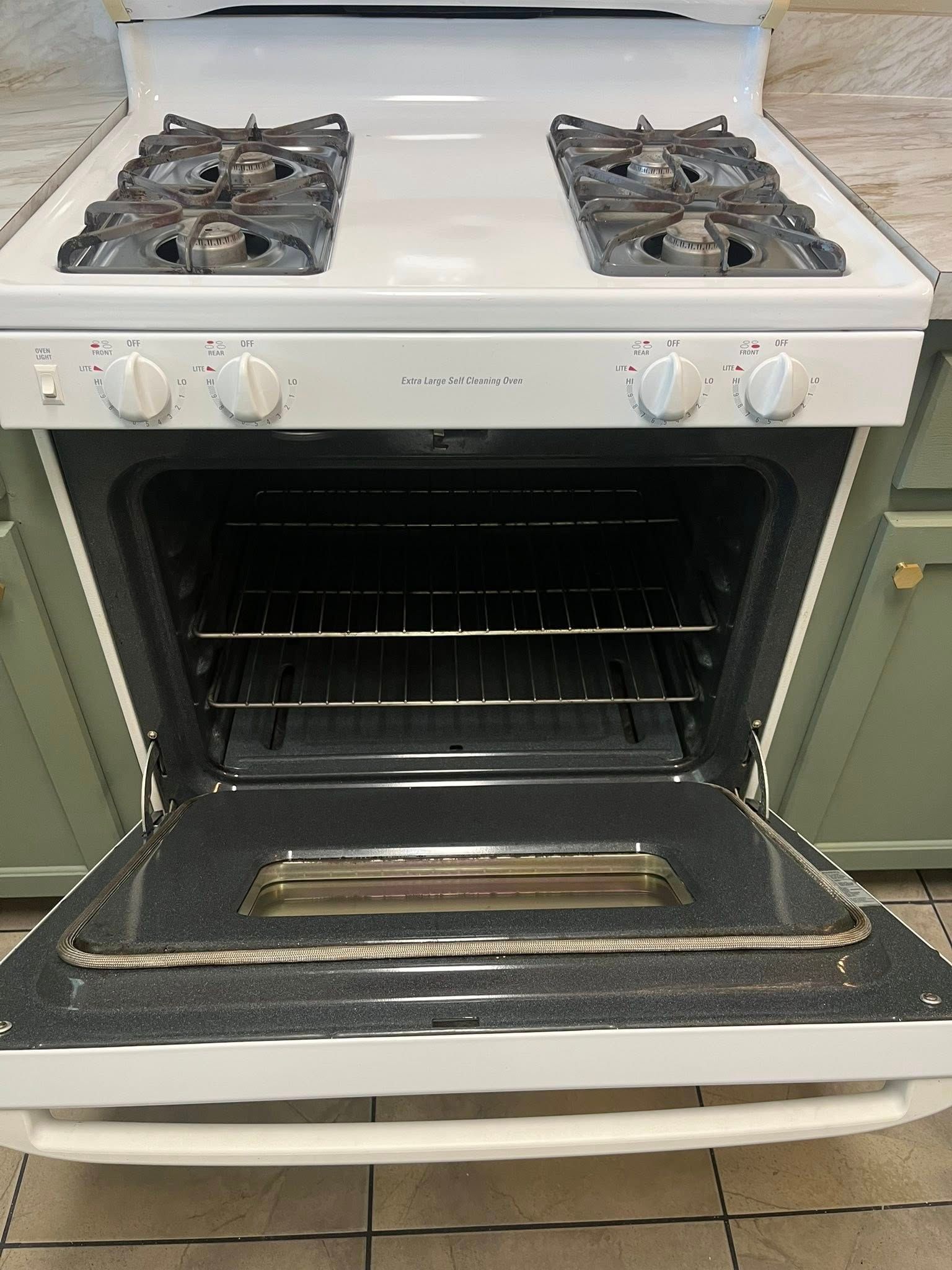 White gas range oven door open, revealing oven interior and racks. Burners and knobs visible.