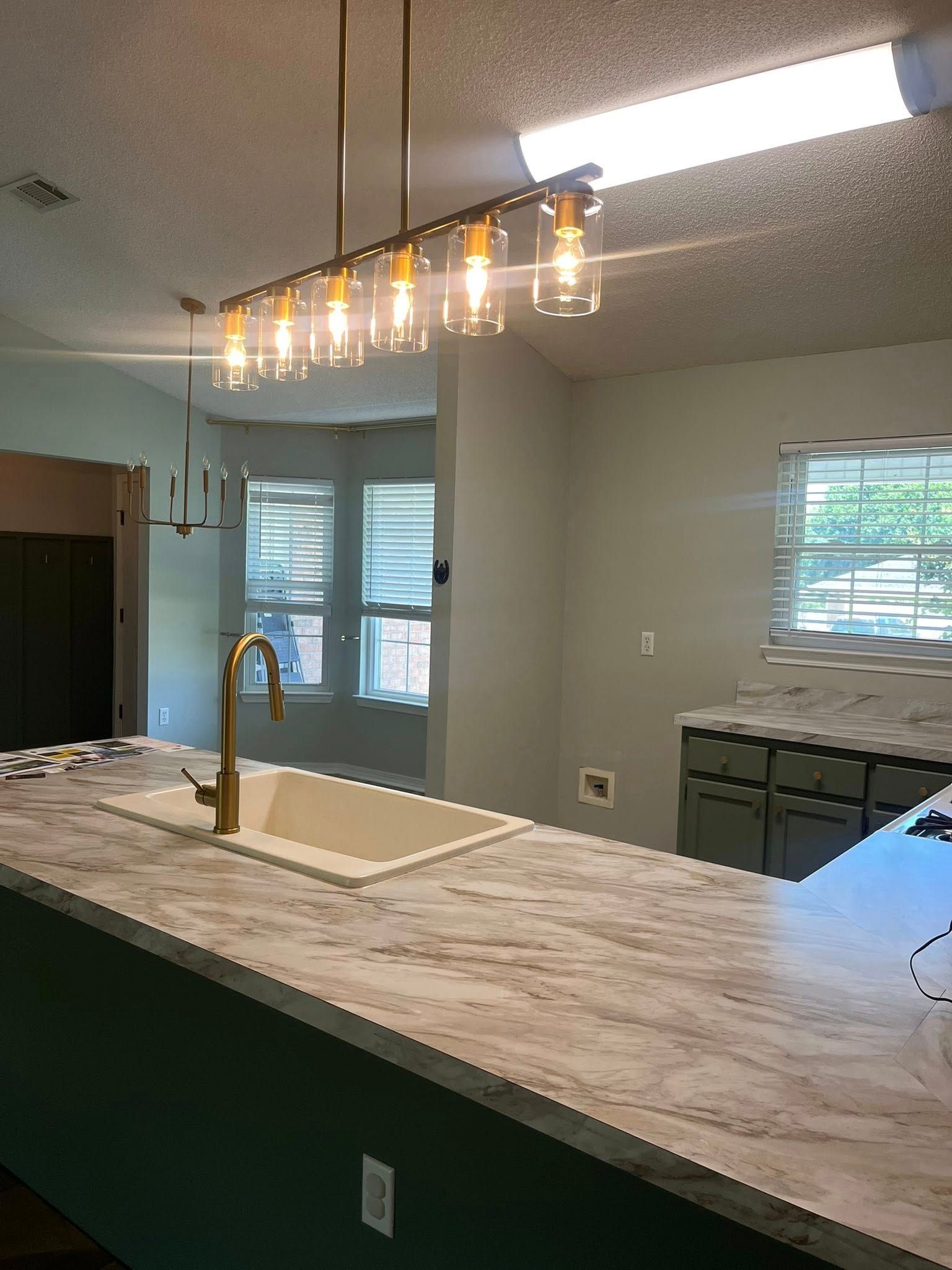 Kitchen with a gold faucet, white countertop, green cabinets, and a hanging light fixture.