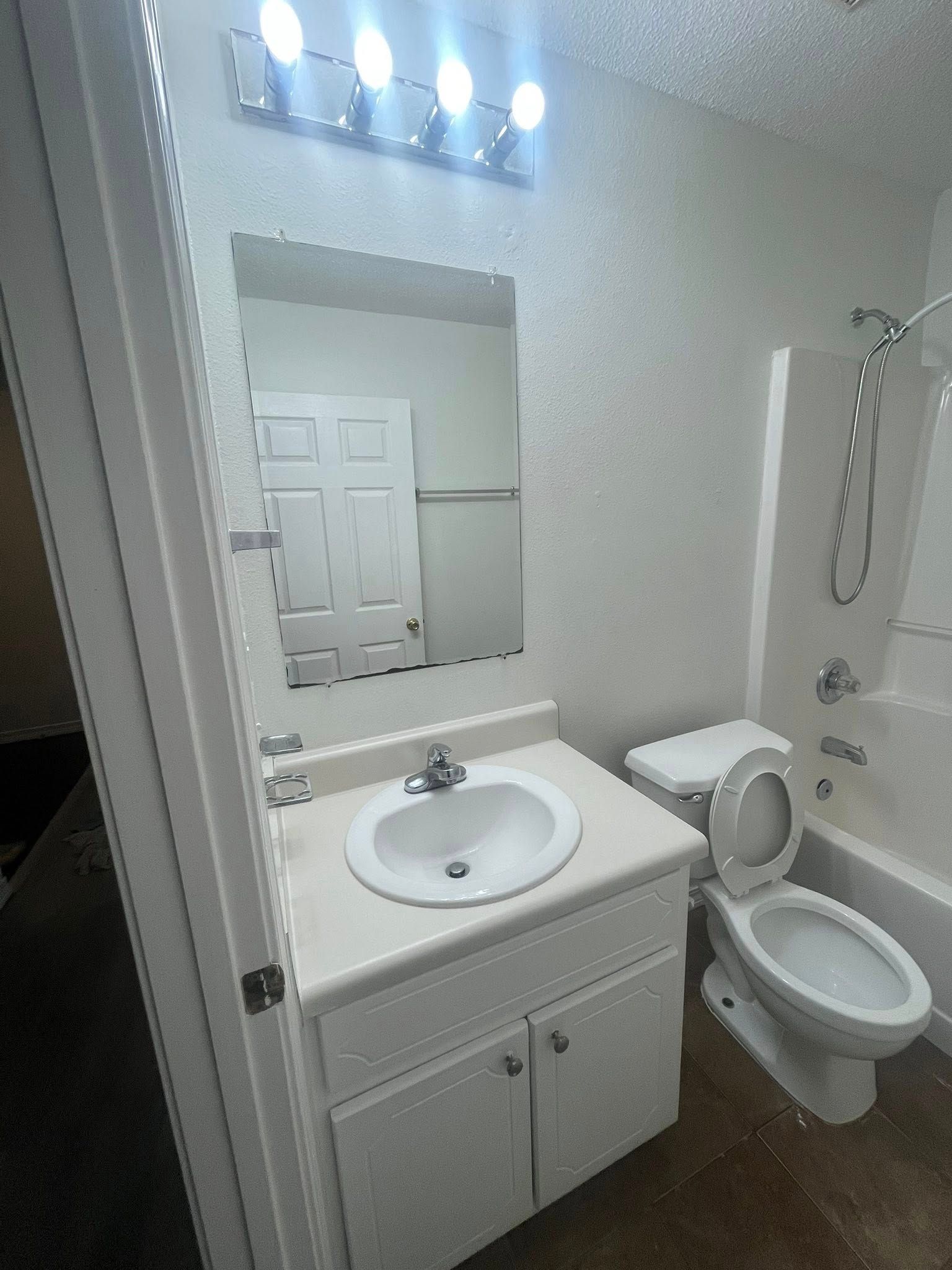 Bathroom with a white vanity, toilet, and bathtub. A mirror and overhead lights are mounted on the wall.
