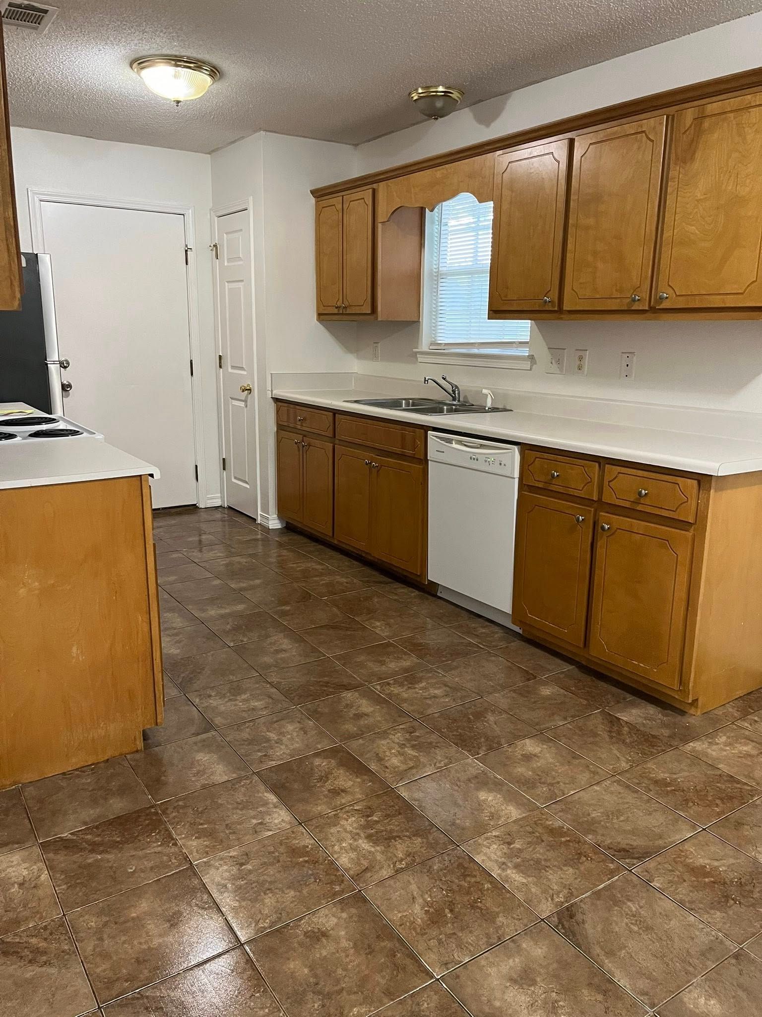 Kitchen with wooden cabinets, white countertop, and tile floor. There is a dishwasher and a doorway.