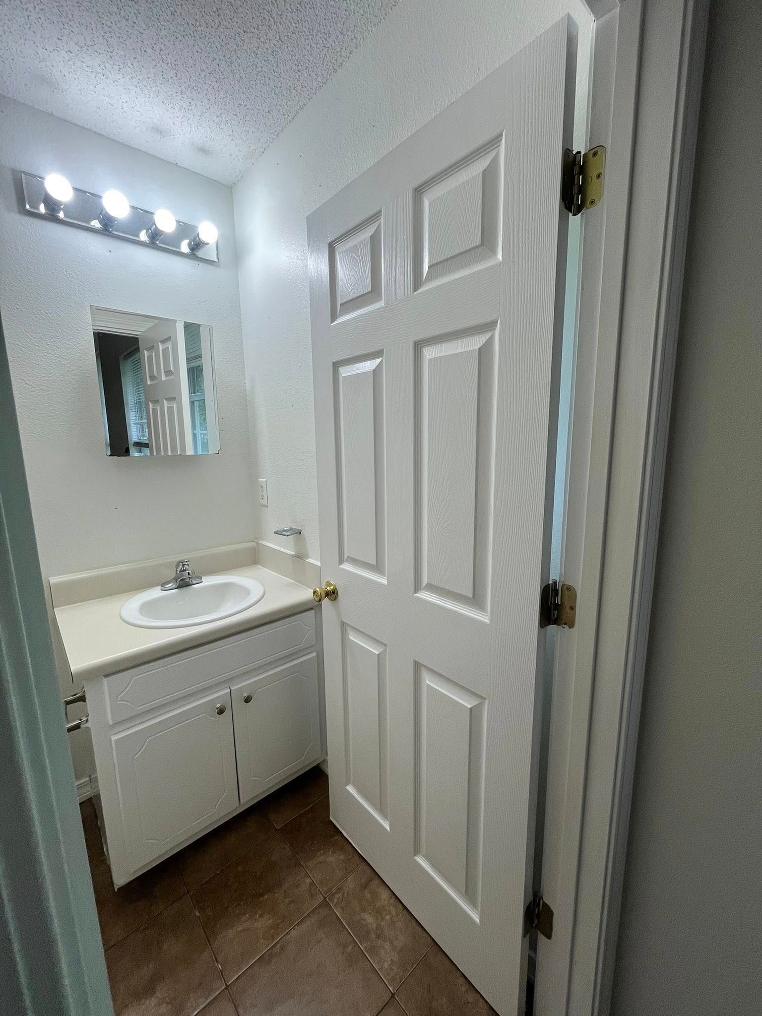 Bathroom with white door, vanity, and mirror; a light fixture above.