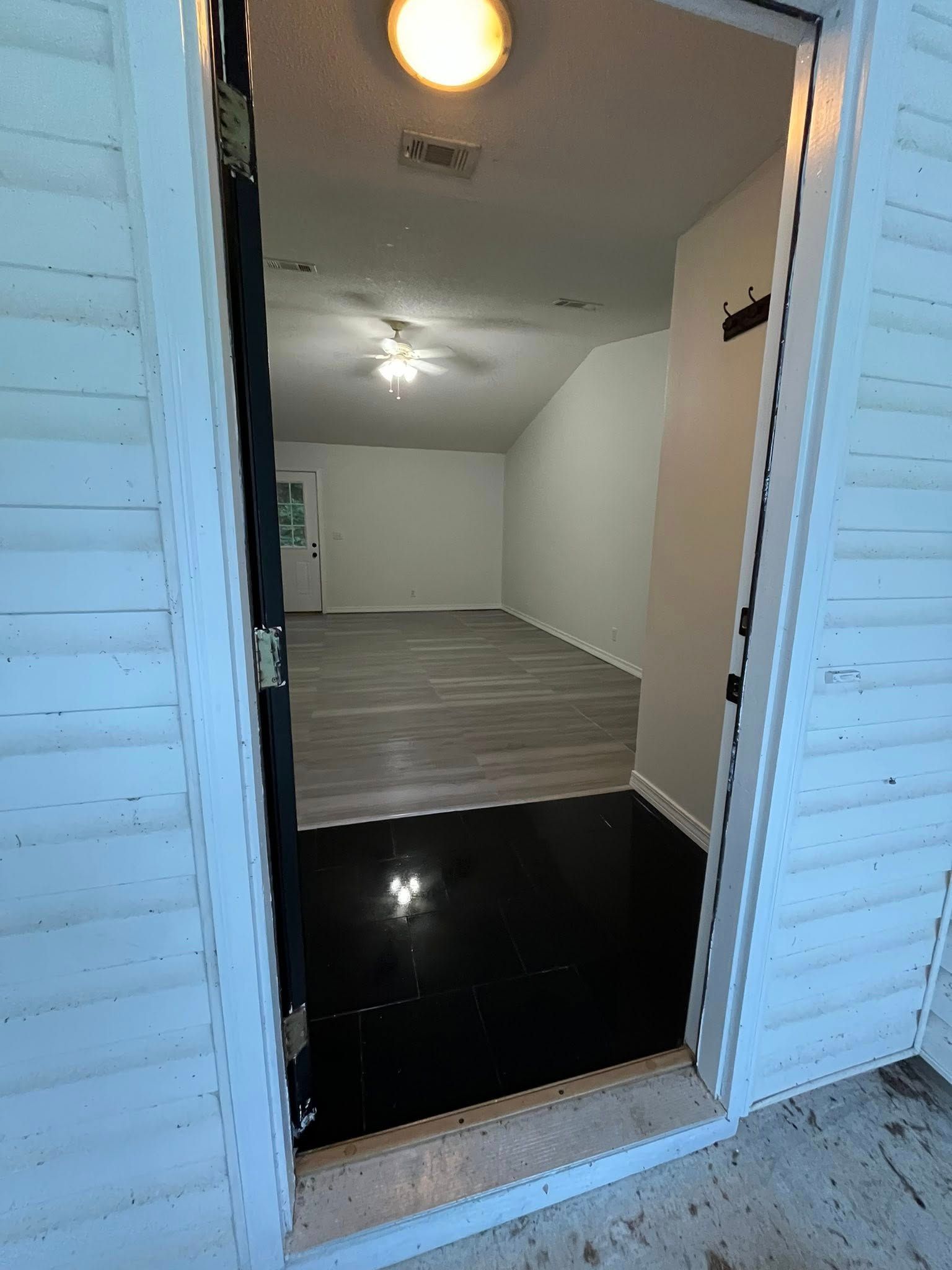 View from an open doorway into a room with gray flooring and white walls, lit by ceiling fixtures.
