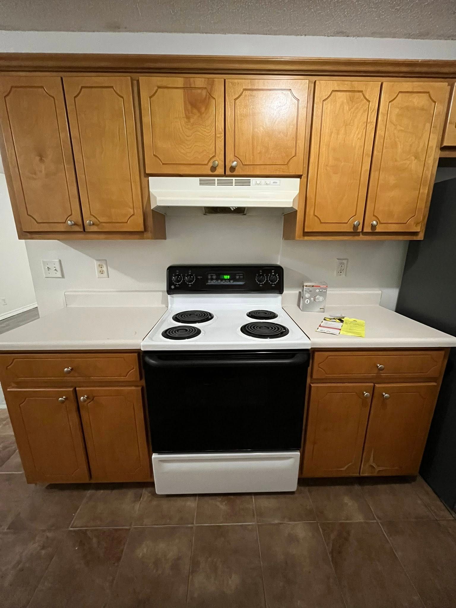 Kitchen with light wood cabinets, white stove, countertops, and range hood.