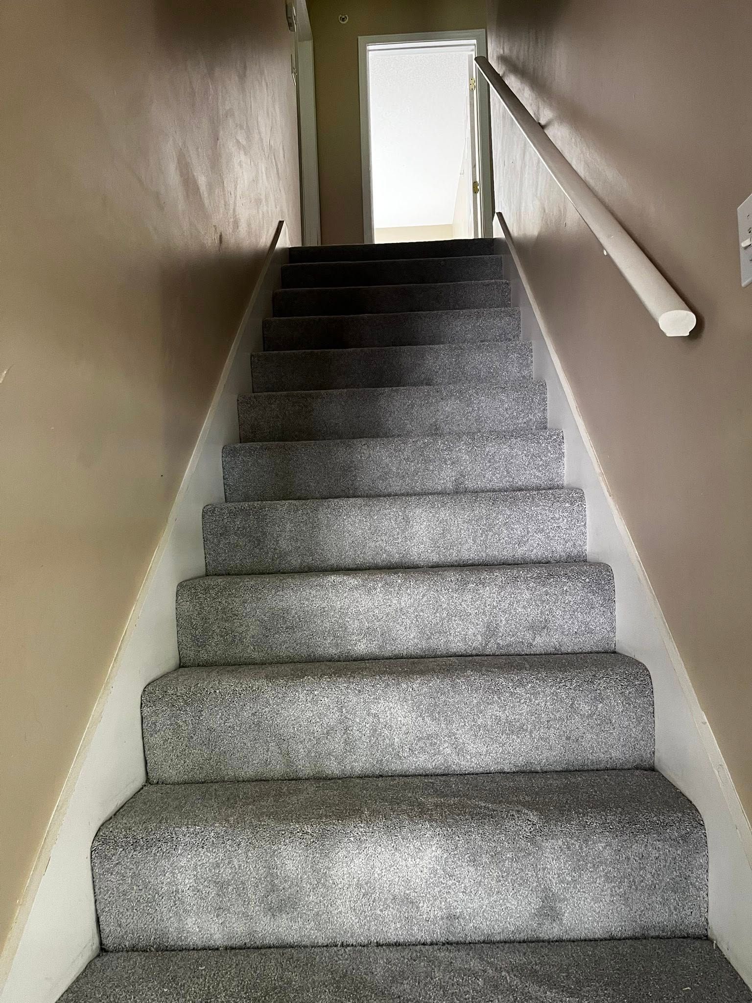 Stairway with gray carpet and white trim.  A white handrail is on the right side. Light enters from upstairs.