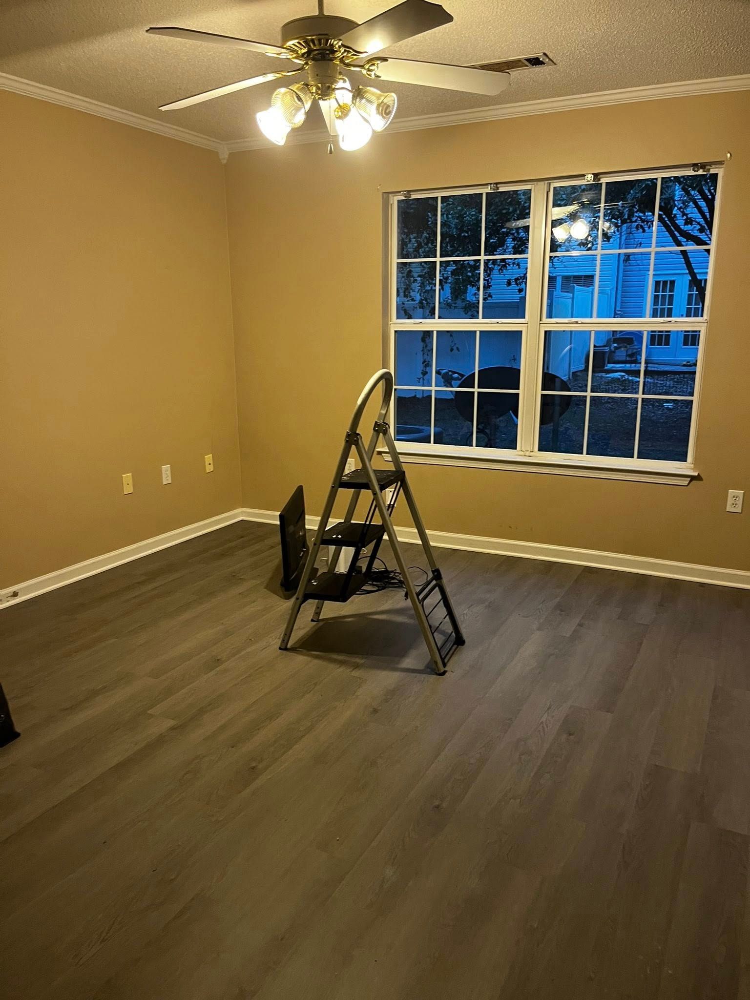 Empty room with ladder, window, ceiling fan, and tan walls.