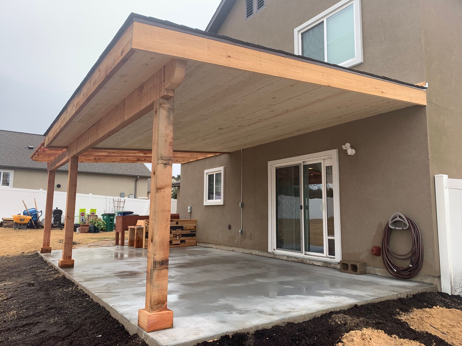 Wooden patio cover attached to a house with outdoor furniture on a concrete patio.