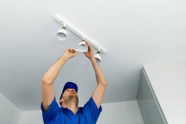 Person in blue shirt and cap installing a track light fixture on a white ceiling.