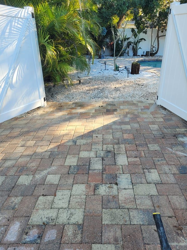 Paver patio with open white gate leading to gravel path and pool.