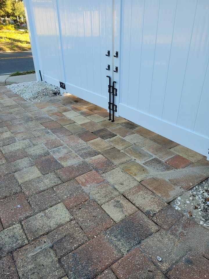 Brick pathway leading to a white vinyl fence with a metal latch.