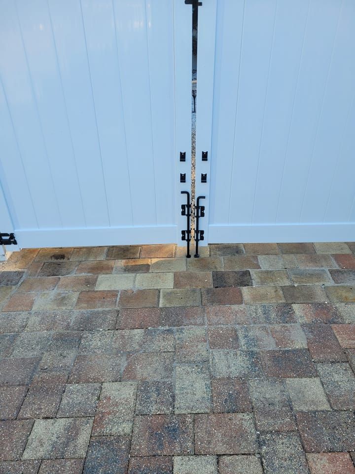 White vinyl gate with black hardware, set on brick pavers.