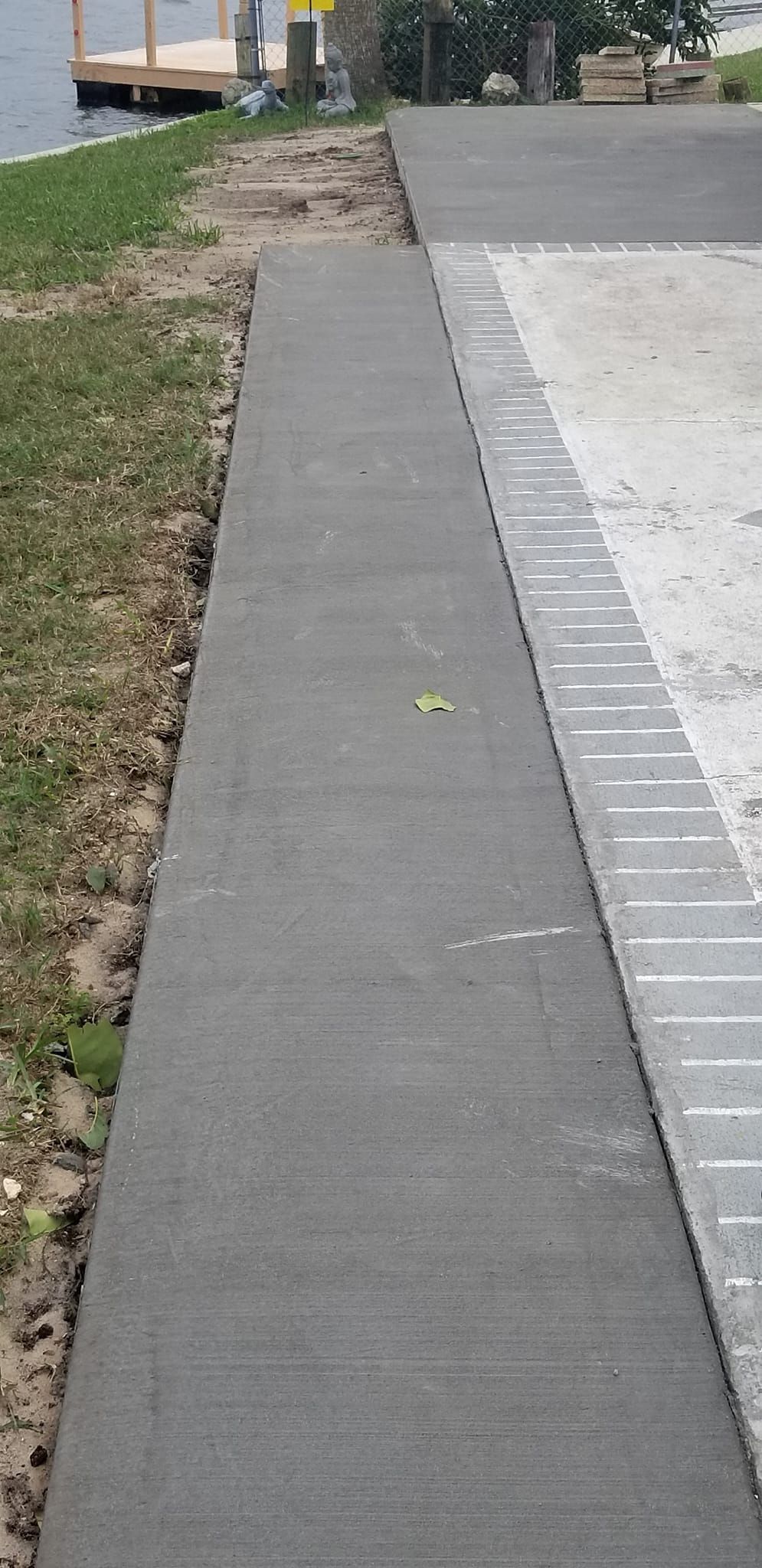 A gray concrete walkway next to grass and a light-colored brick paved area, near a body of water.