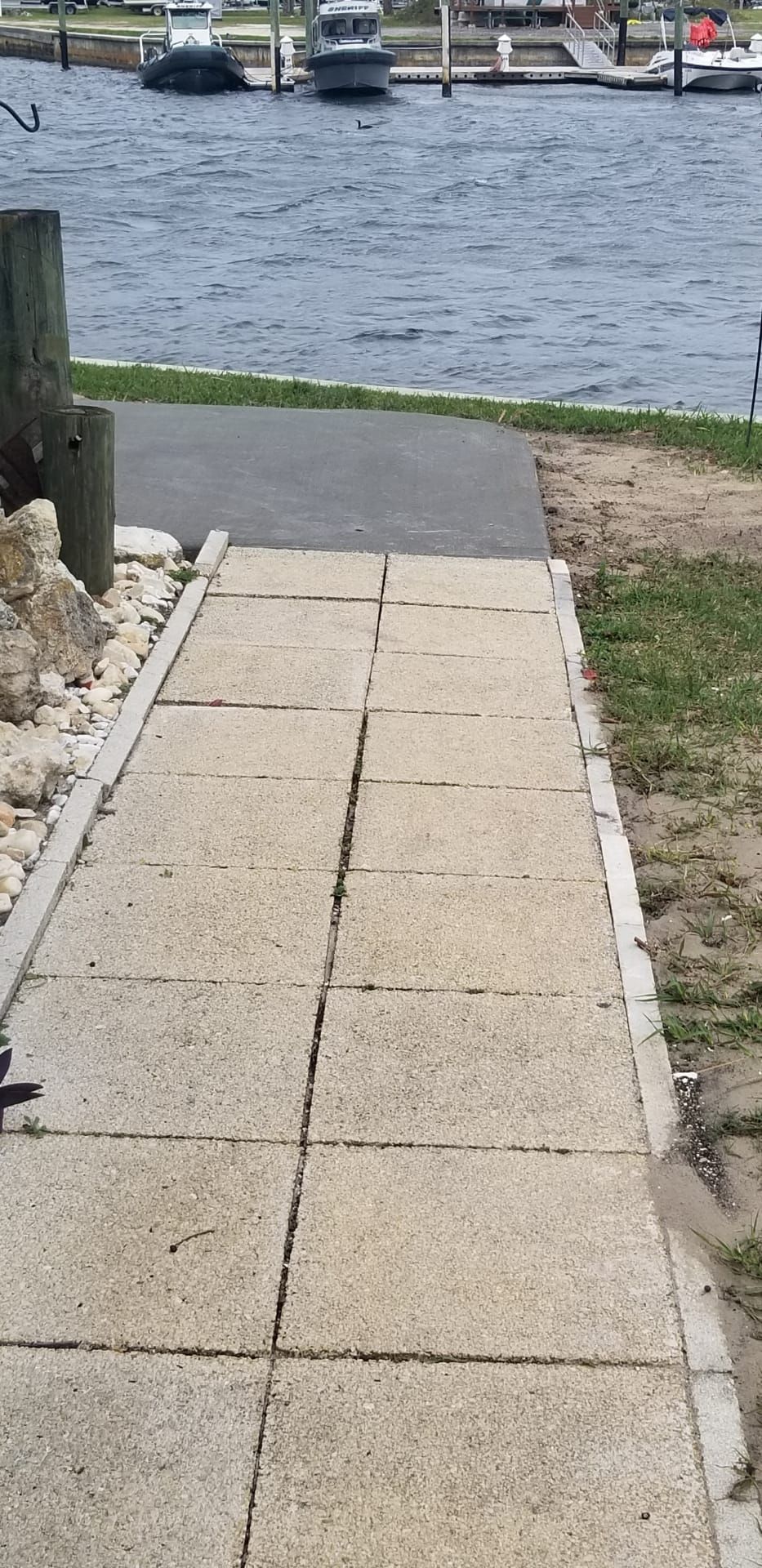 Concrete walkway leading down to a waterfront. Boats are docked in the background, with water on either side.