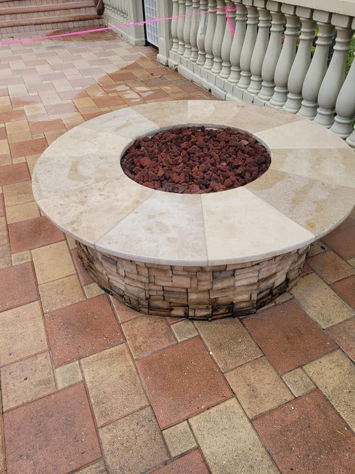 Circular stone fire pit on a patio, with red stones inside the fire ring.