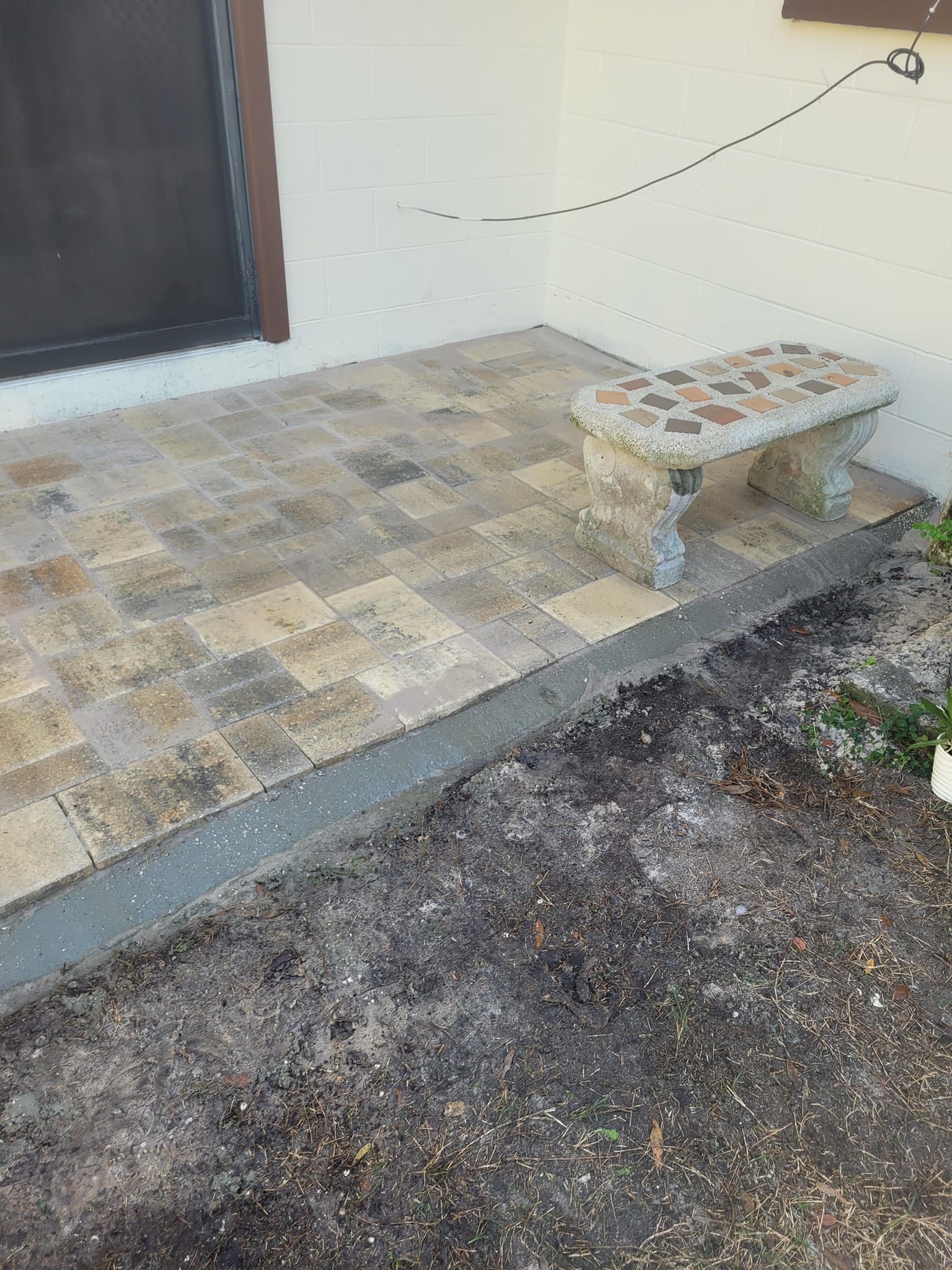 Stone patio with bench next to a door, small plants in the foreground.