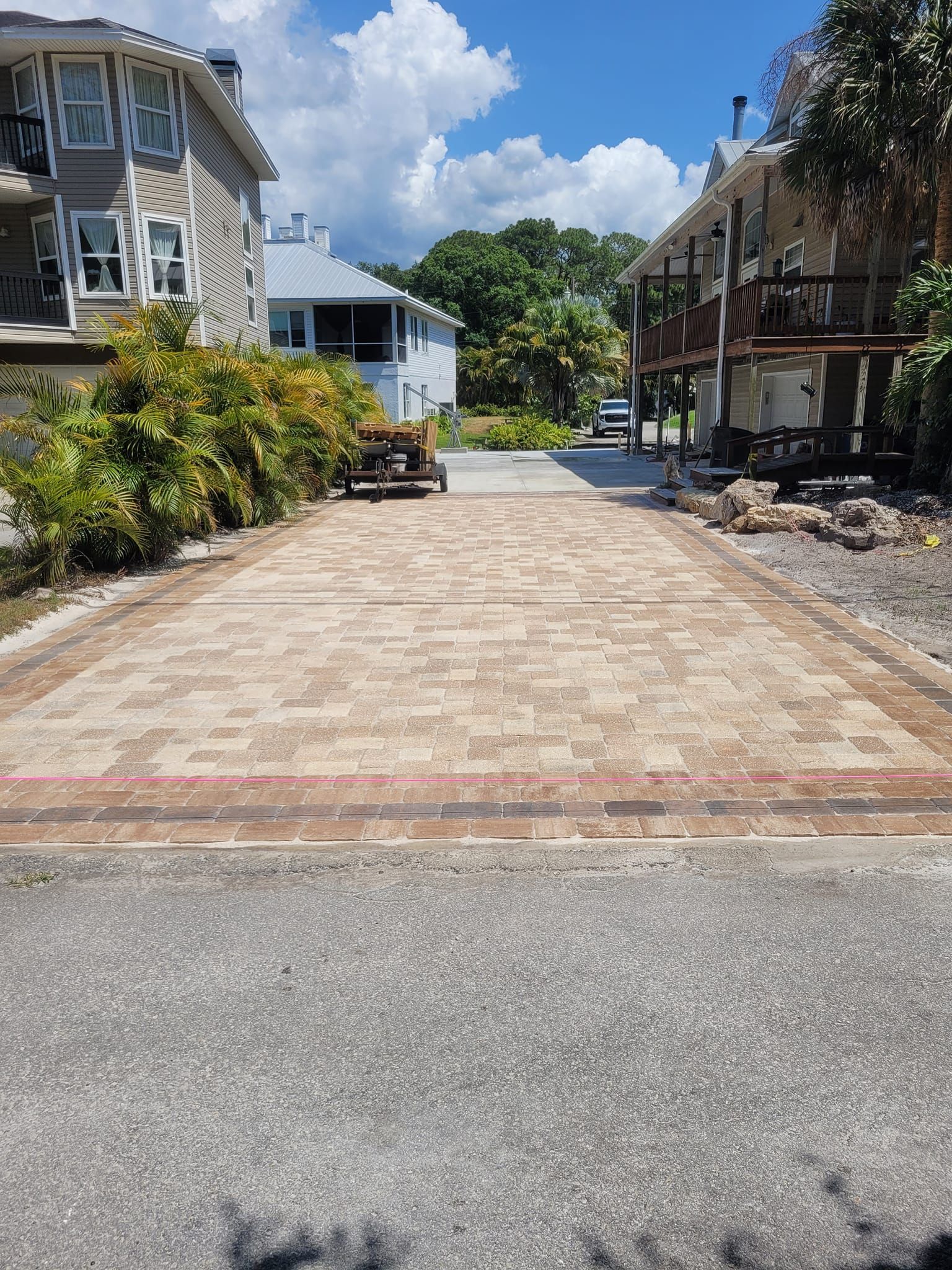 Brick paved driveway between two buildings, partially visible street, sunny day.