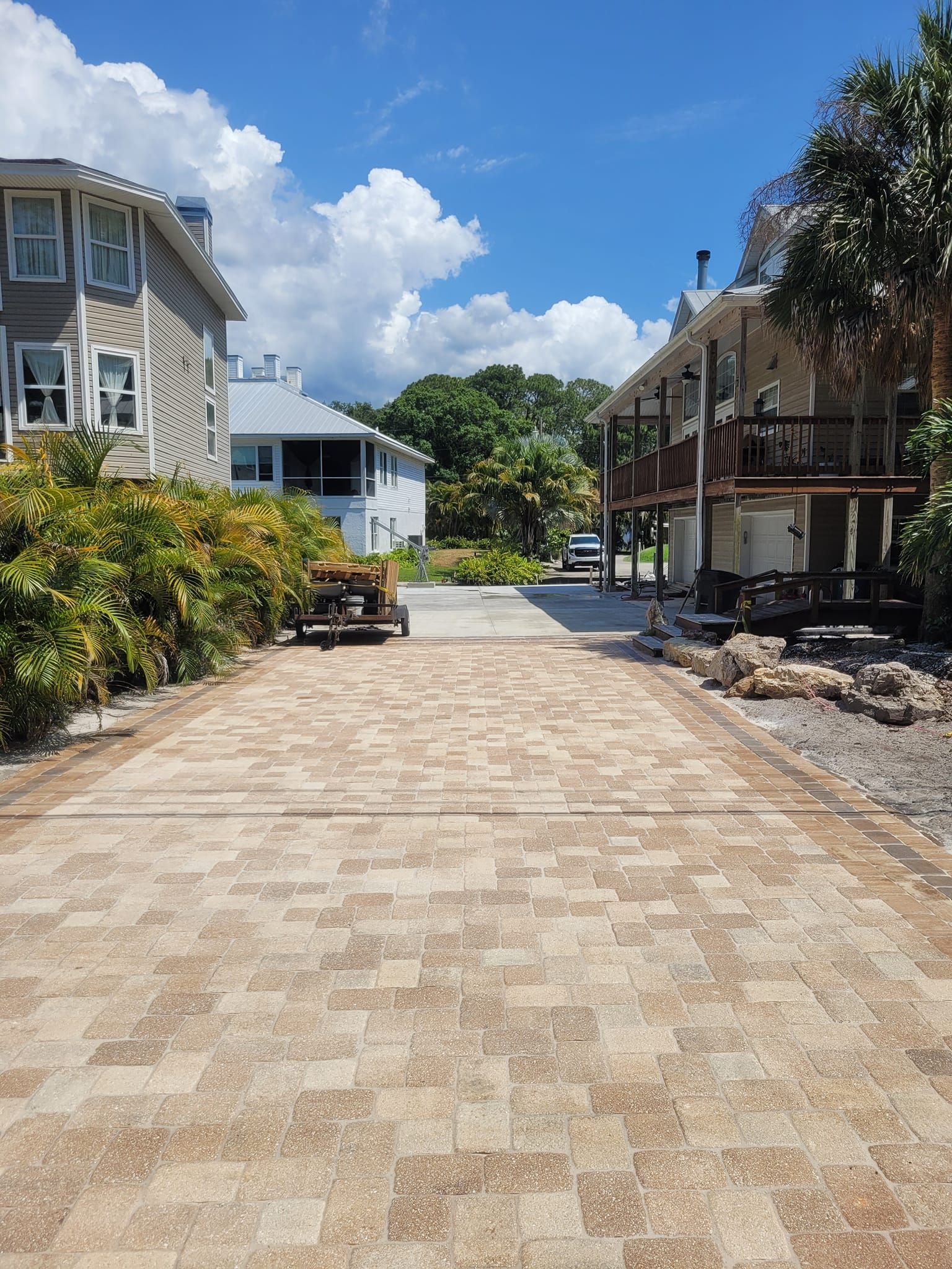 Brick walkway between houses, sunny day, blue sky, trees in background.