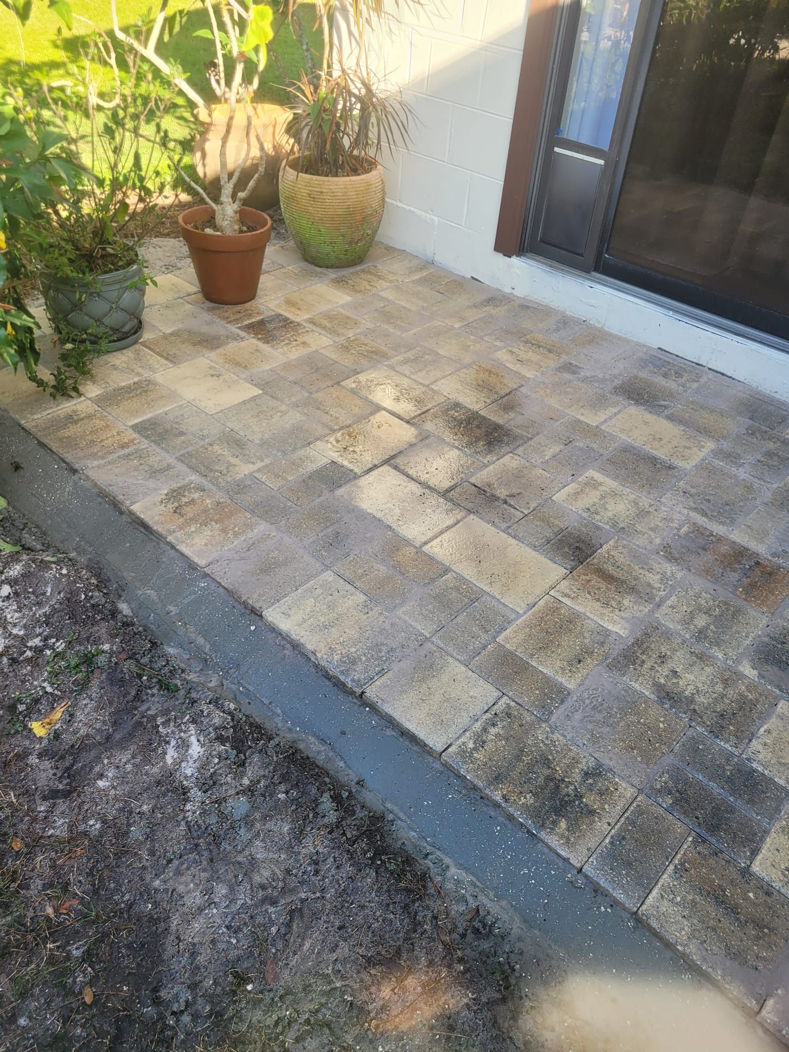 Brick paved patio with potted plants in front of a house next to a sliding glass door.