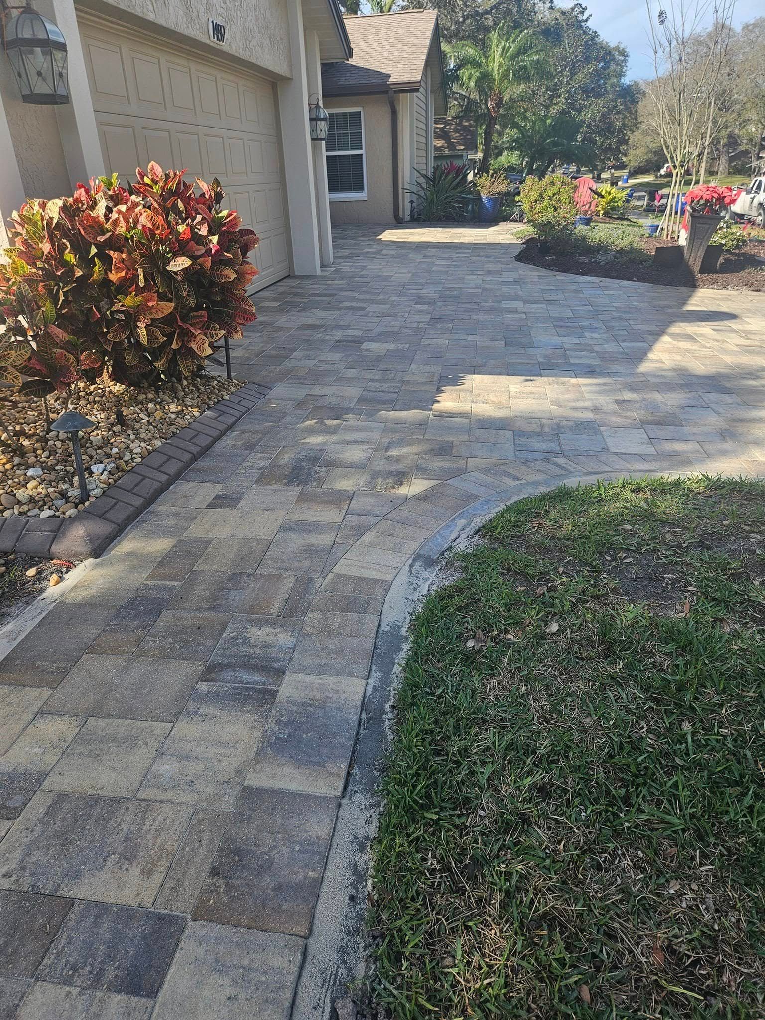 Brick pathway leading to a house, with green grass and colorful plants on either side.