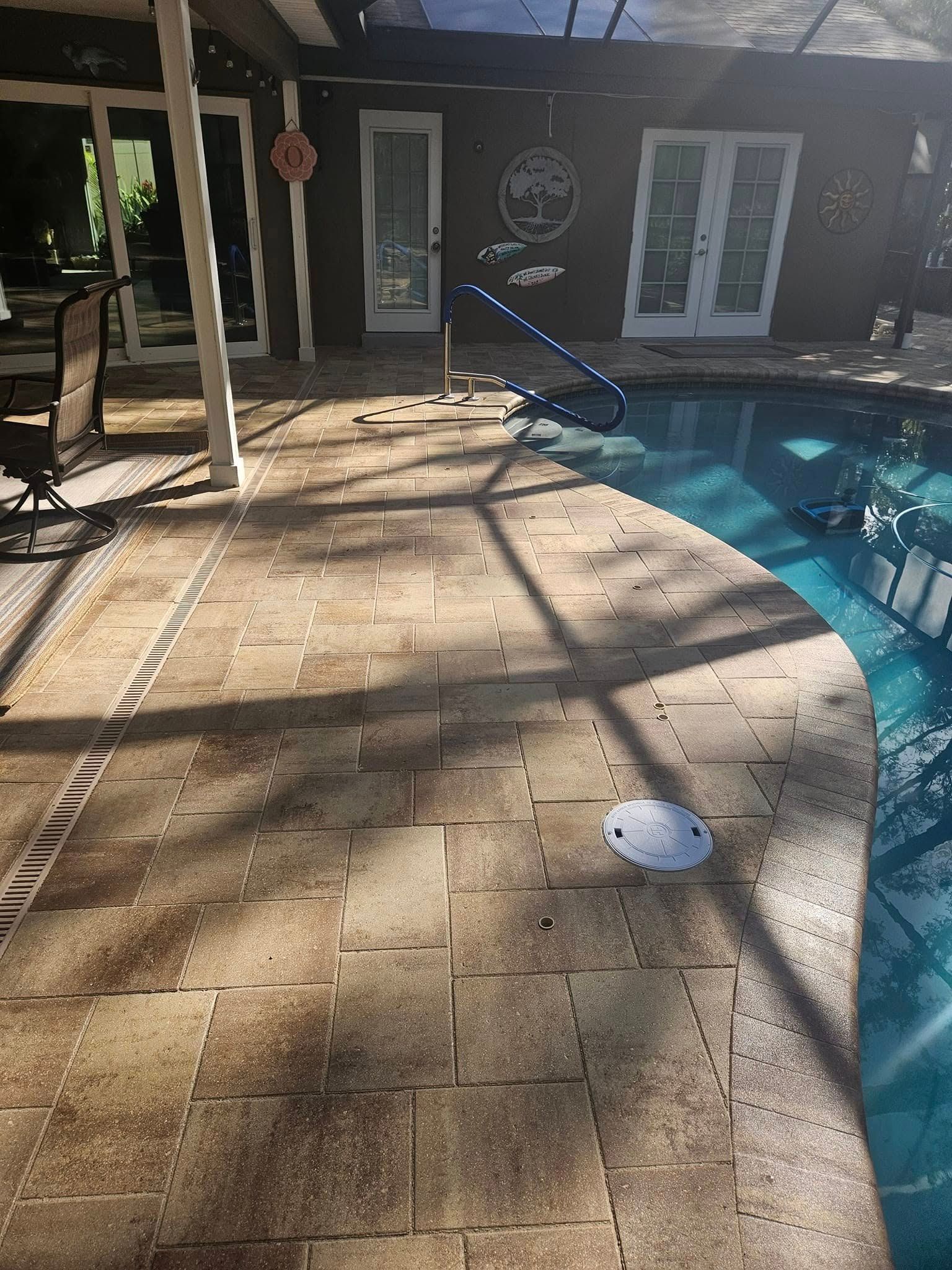 Poolside scene with brick patio and pool. A building with French doors is in the background.