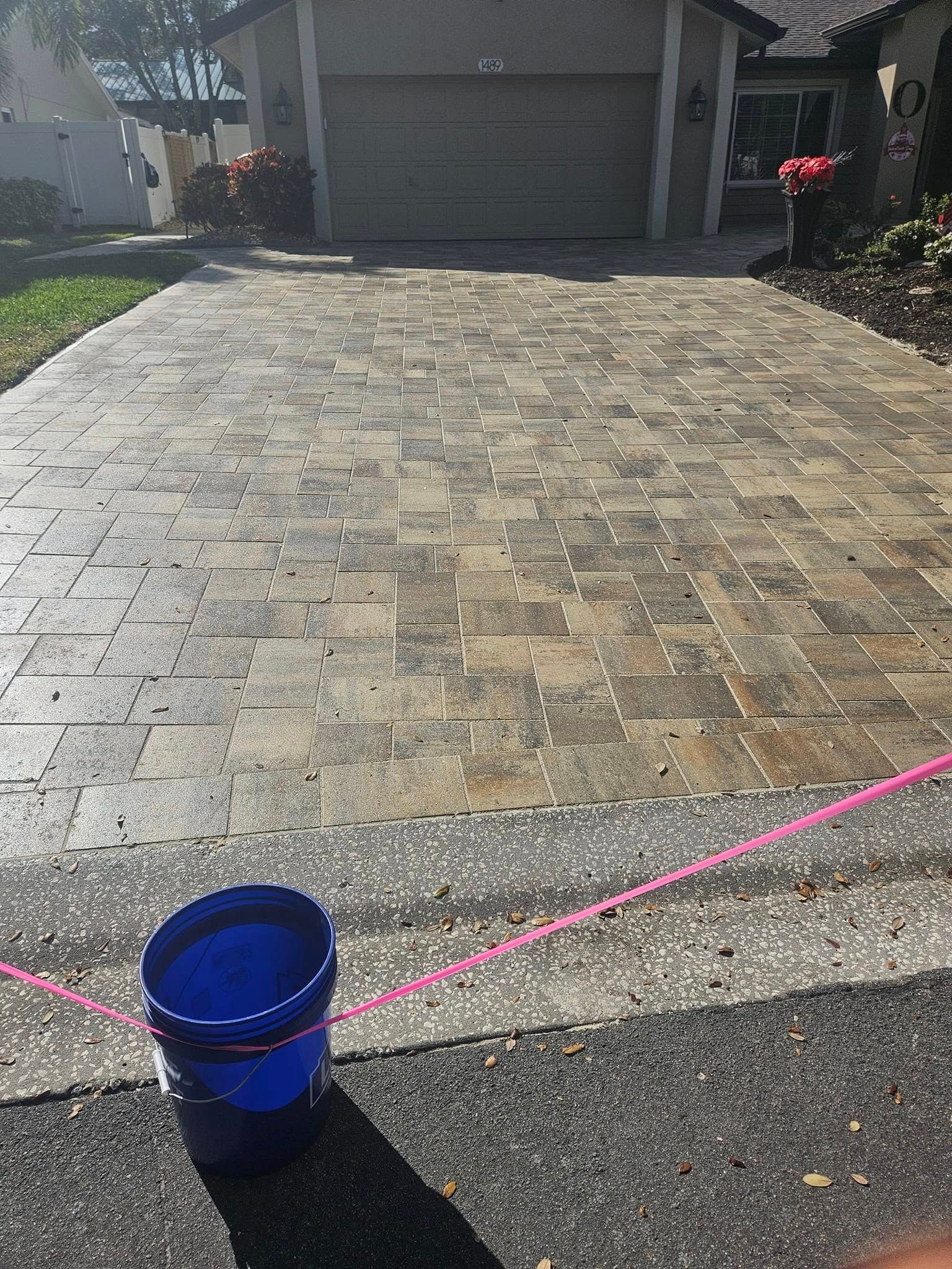 Brick driveway leading to a garage. A blue bucket sits in the foreground.