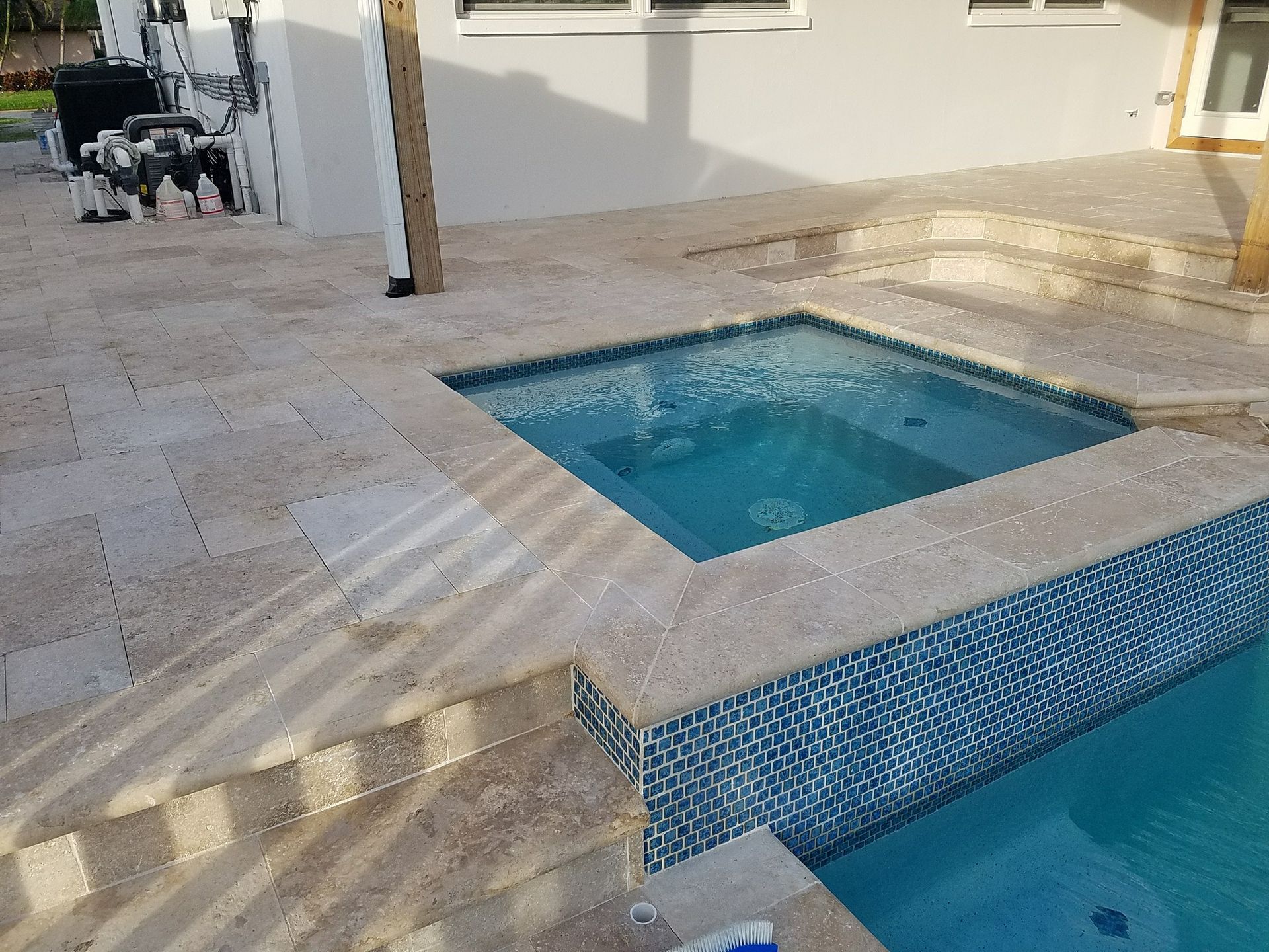 Hot tub and pool with blue tile surround, beige stone patio.