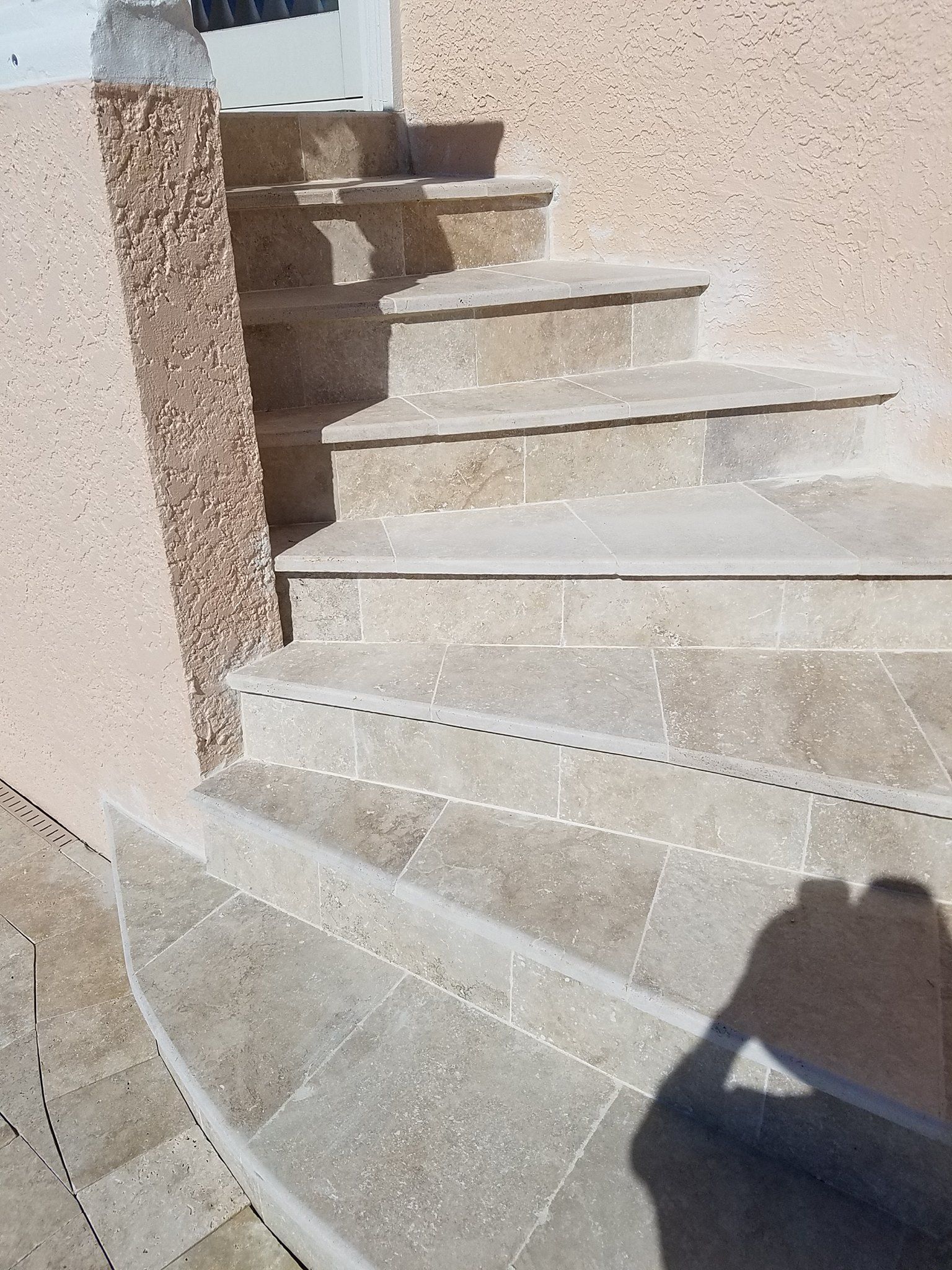 Stone steps leading upwards, beside a textured wall and corner. Shadow of a person visible.