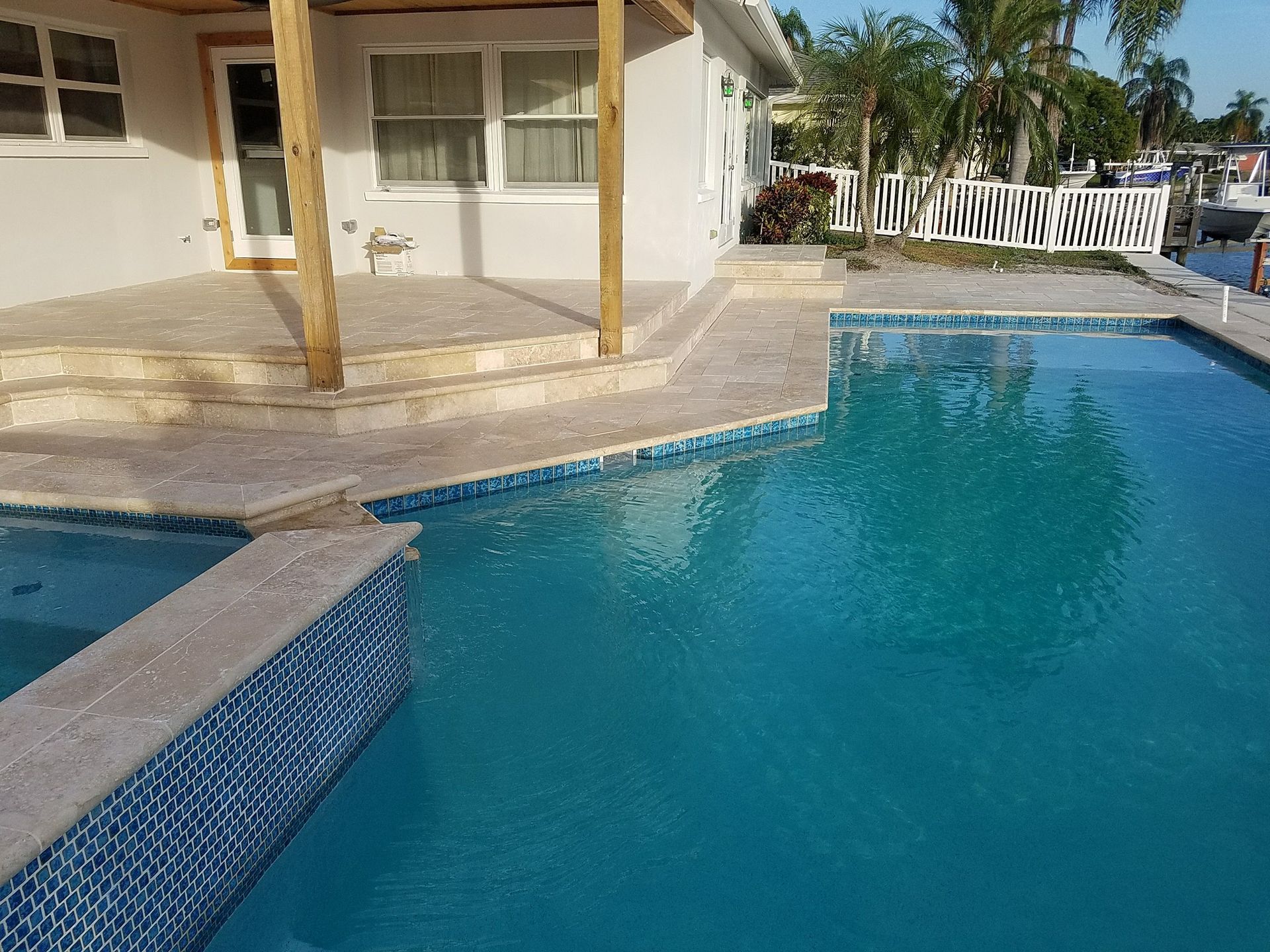 Pool with blue water and tiled edges, next to a house with porch and steps.
