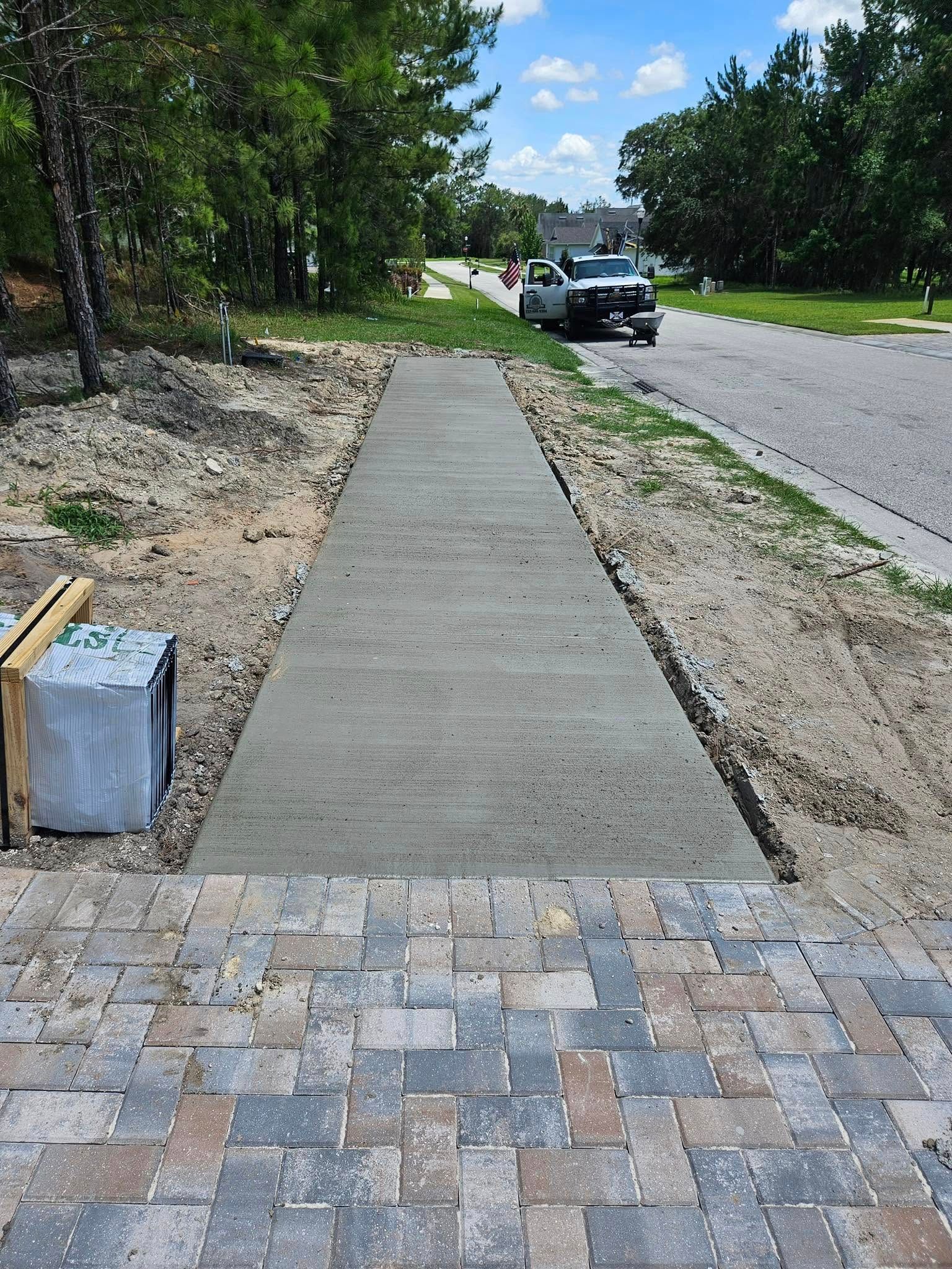 Newly poured concrete walkway leading from a brick-paved landing to a street.