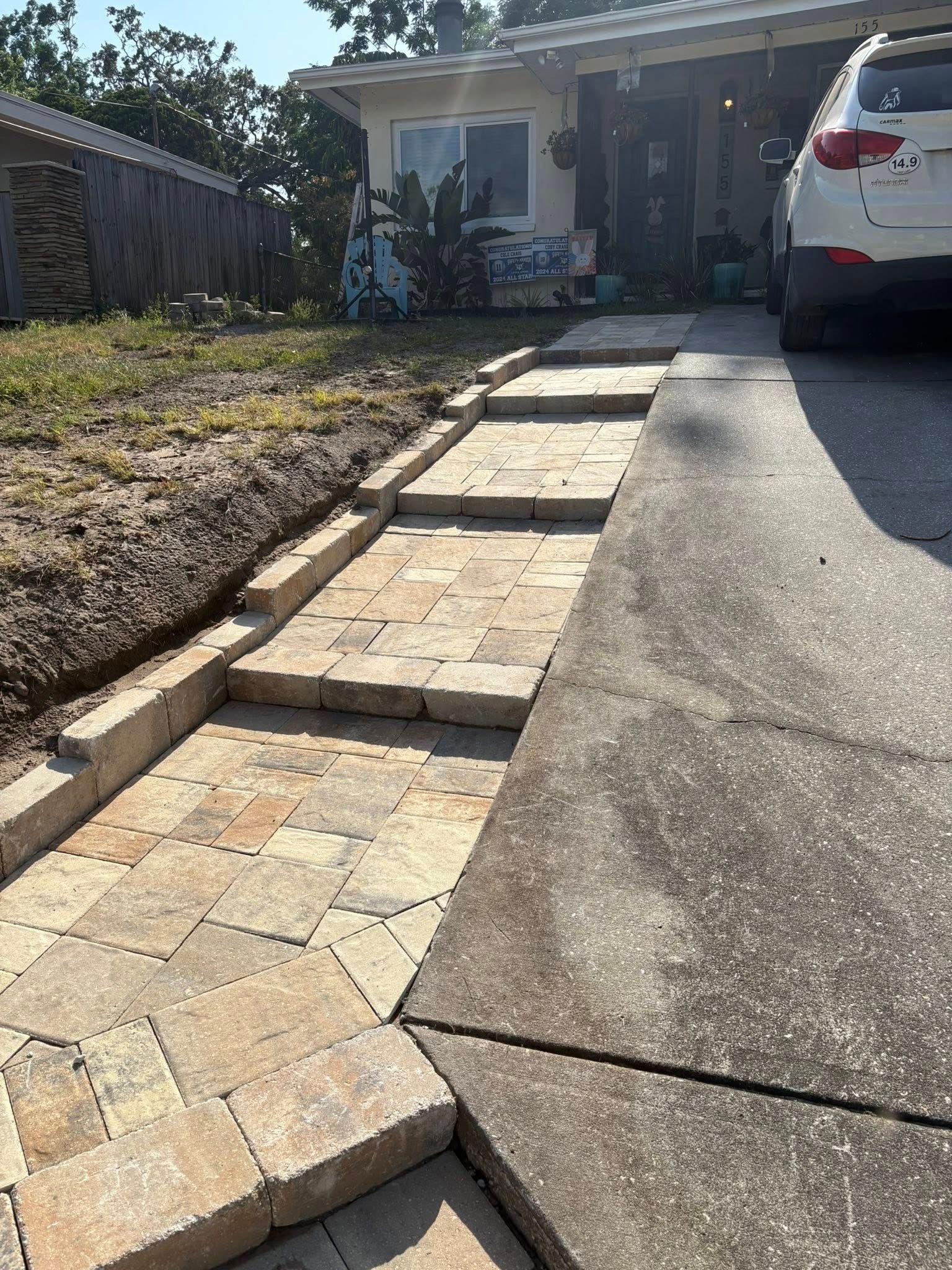 Brick pathway with steps alongside a driveway leading to a house.