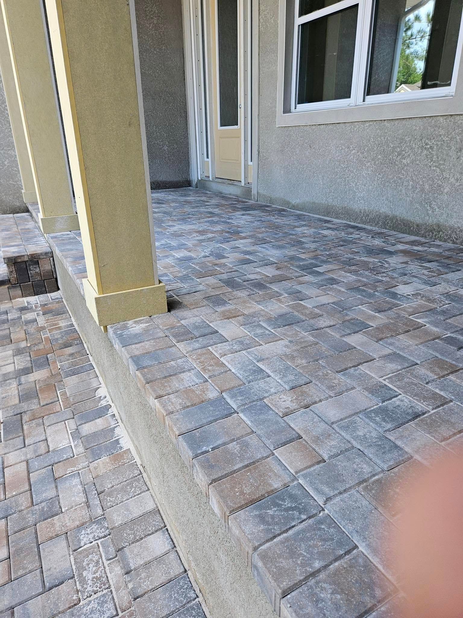 Exterior patio paved with interlocking bricks, featuring a column and a building in the background.