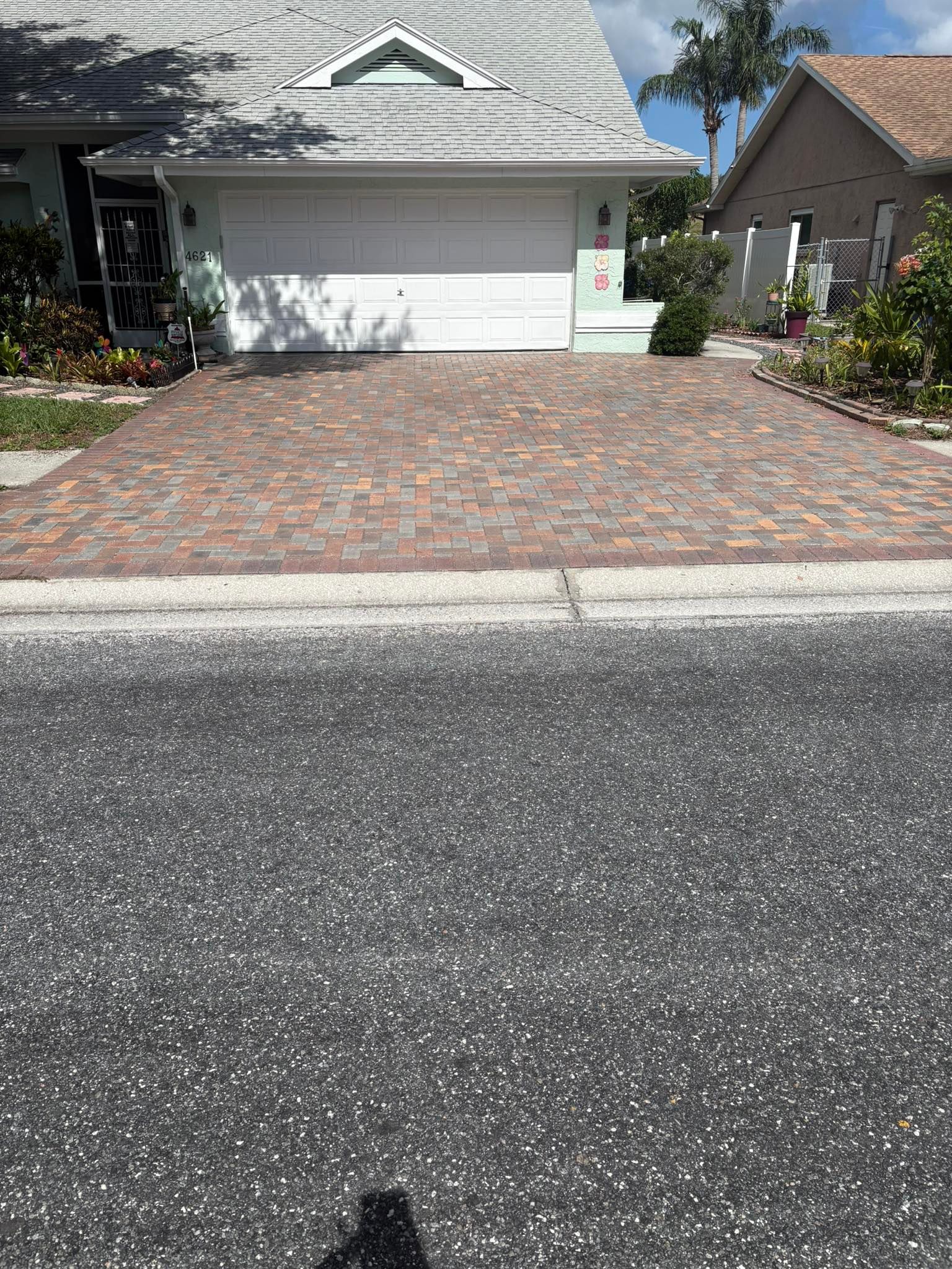 Brick driveway in front of a house with a white garage door, palm trees visible.