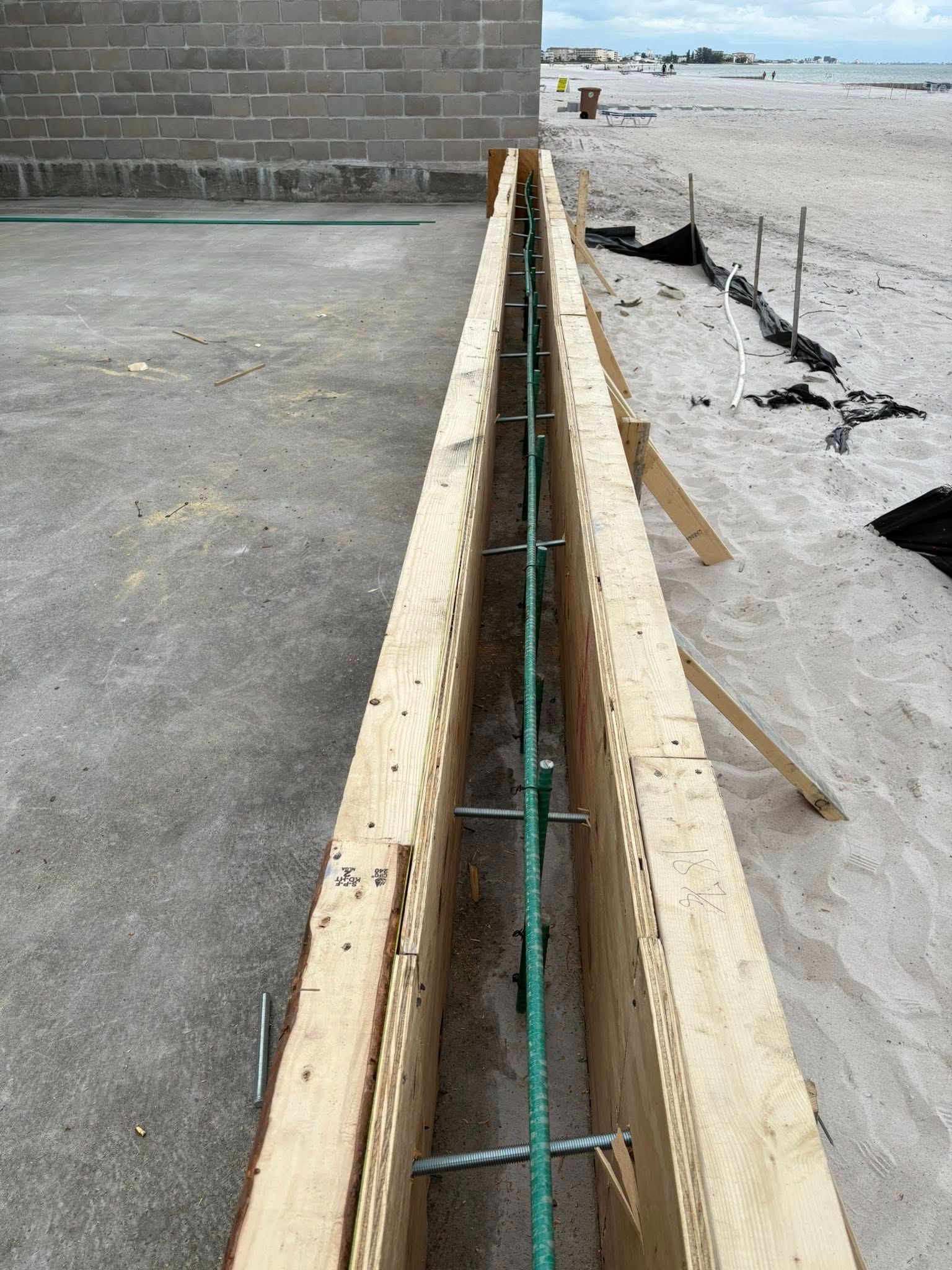 Wooden frame with green rebar on a sandy beach.