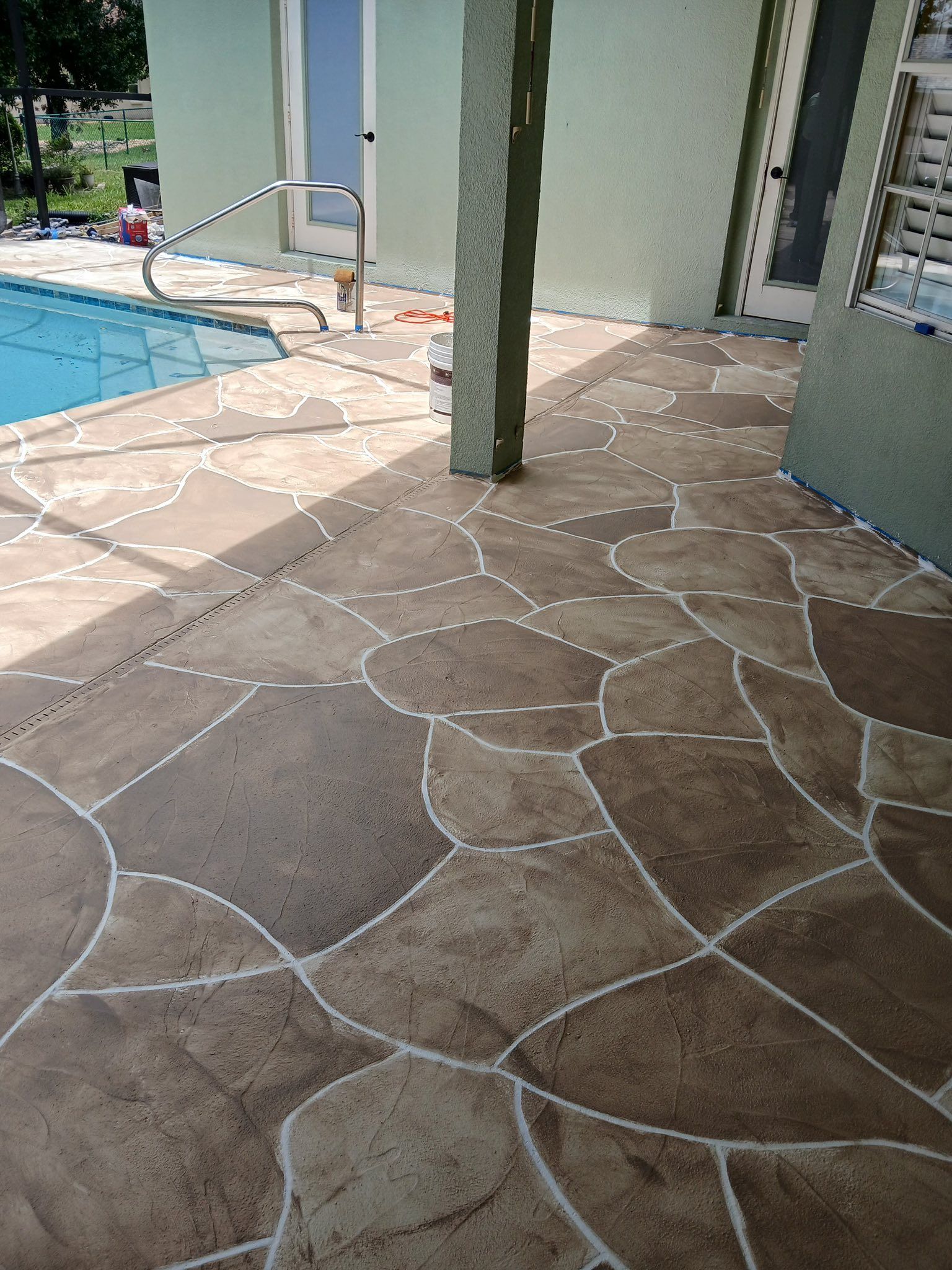Concrete patio with a flagstone design, bordering a swimming pool.