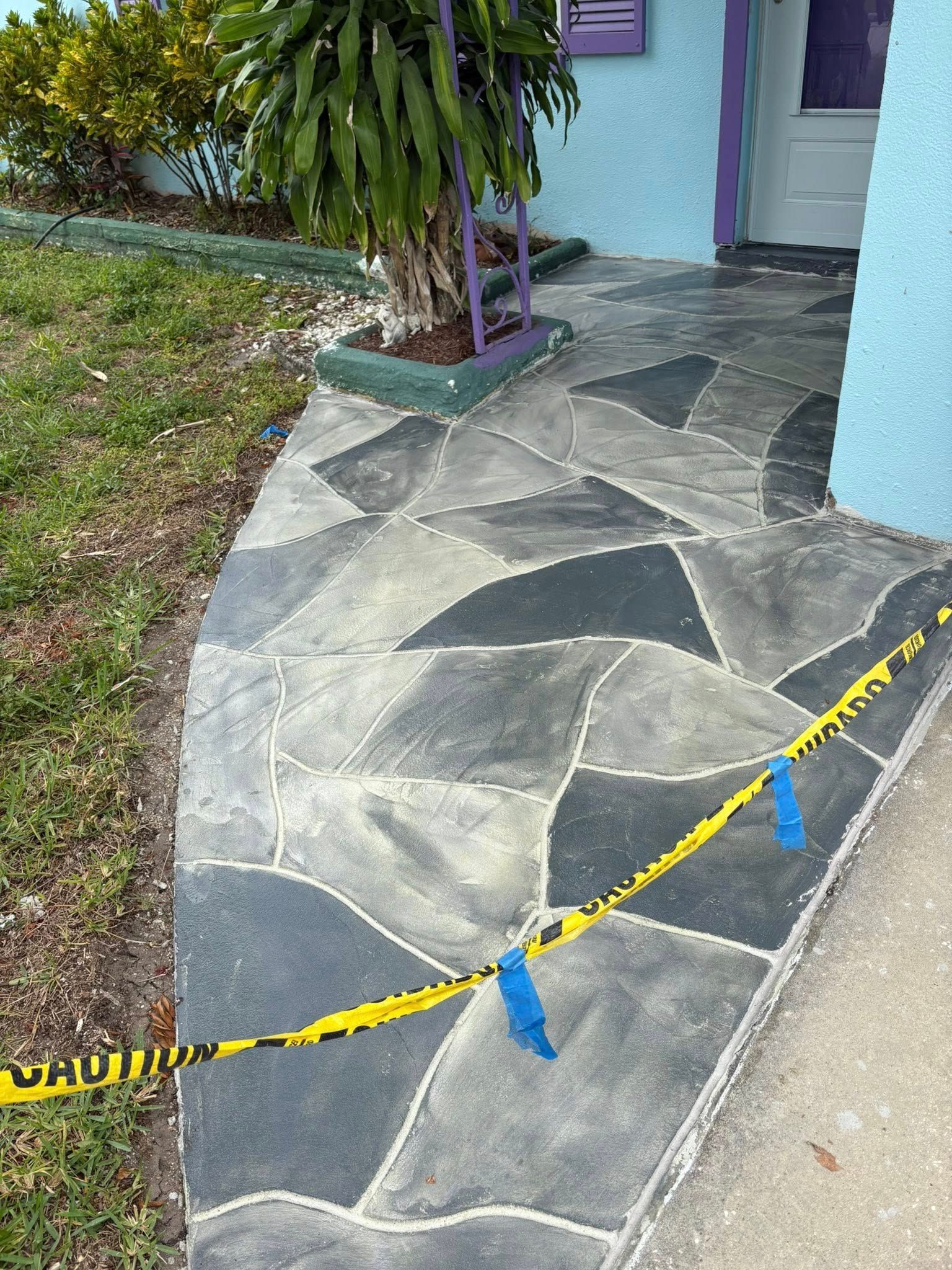 Mosaic-patterned walkway marked with caution tape, leading to a blue house with a purple door.