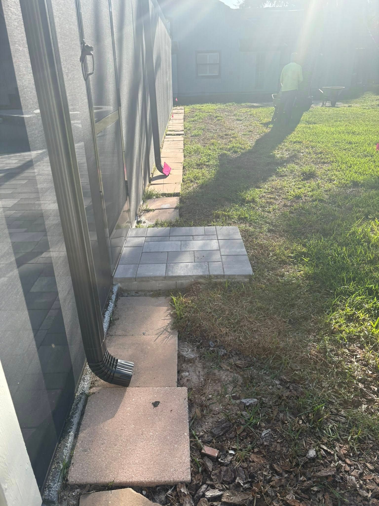 Stone path along a screened enclosure, leading into a grassy yard. Sun illuminates the scene.