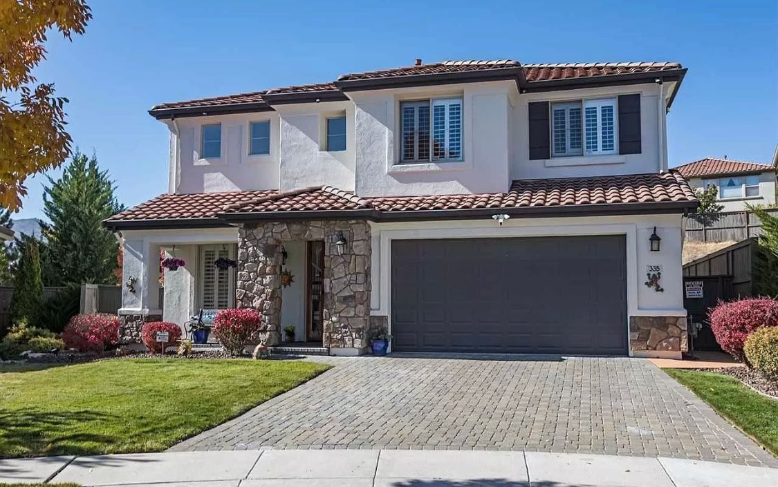 A large white house with a gray garage door is sitting on top of a lush green lawn.