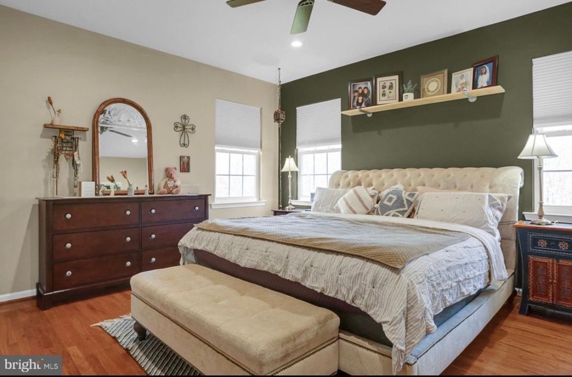 A bedroom with a large bed , dresser , mirror and ceiling fan.