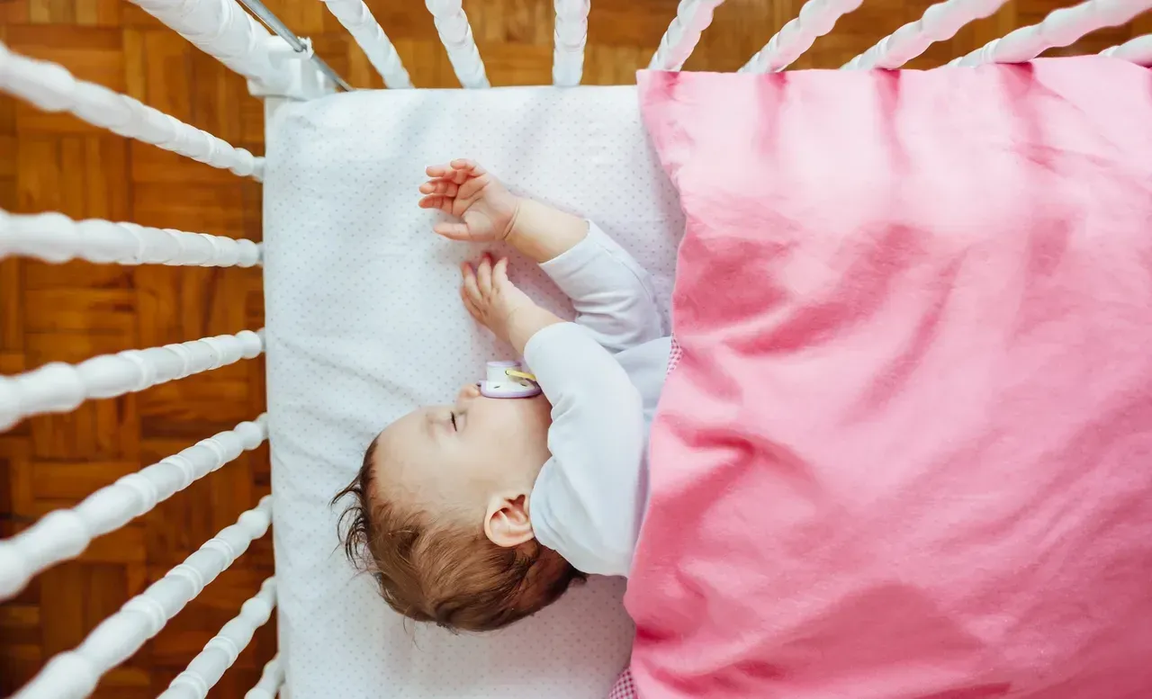 A baby is sleeping in a crib with a pacifier in his mouth.