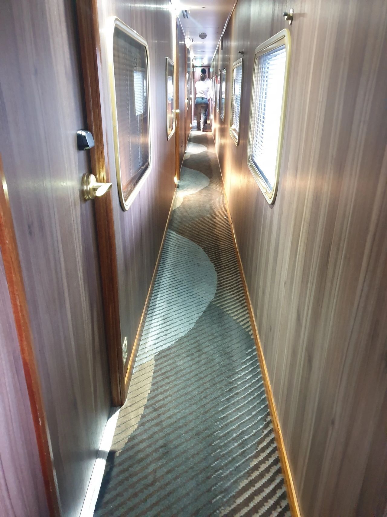 A person is walking down a long hallway with a striped carpet.