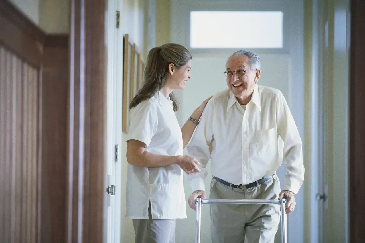 A nurse is helping an elderly man walk with a walker.