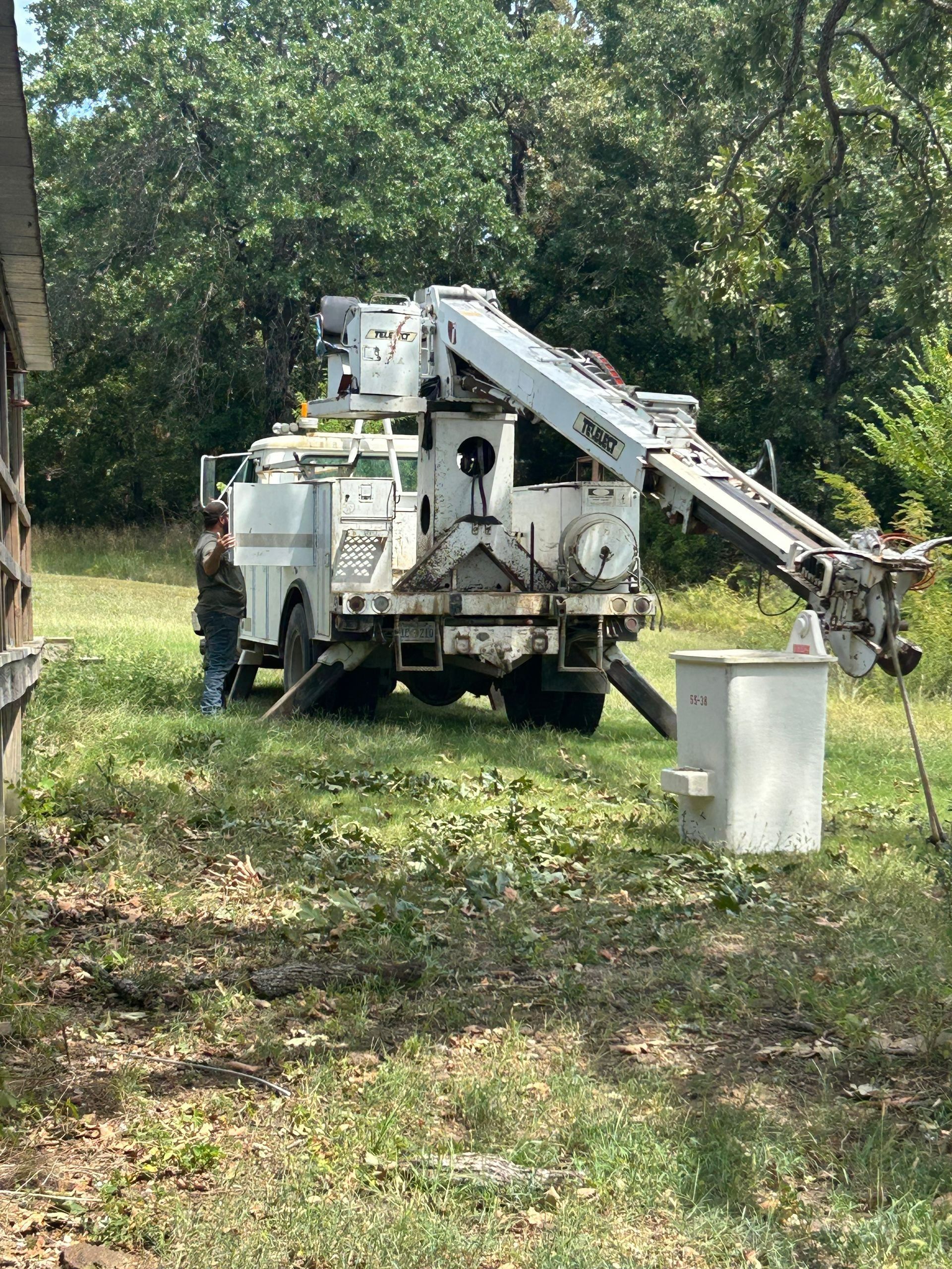Utility truck with crane by a building and cabinet in grassy area. A worker stands nearby.