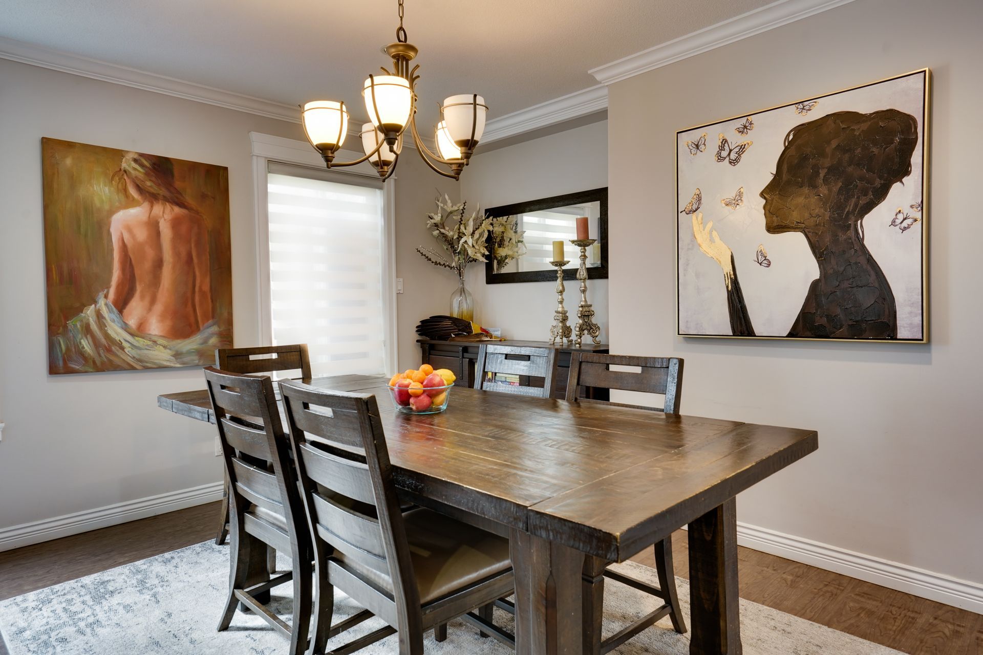 A dining room with a wooden table and chairs and two paintings on the wall.
