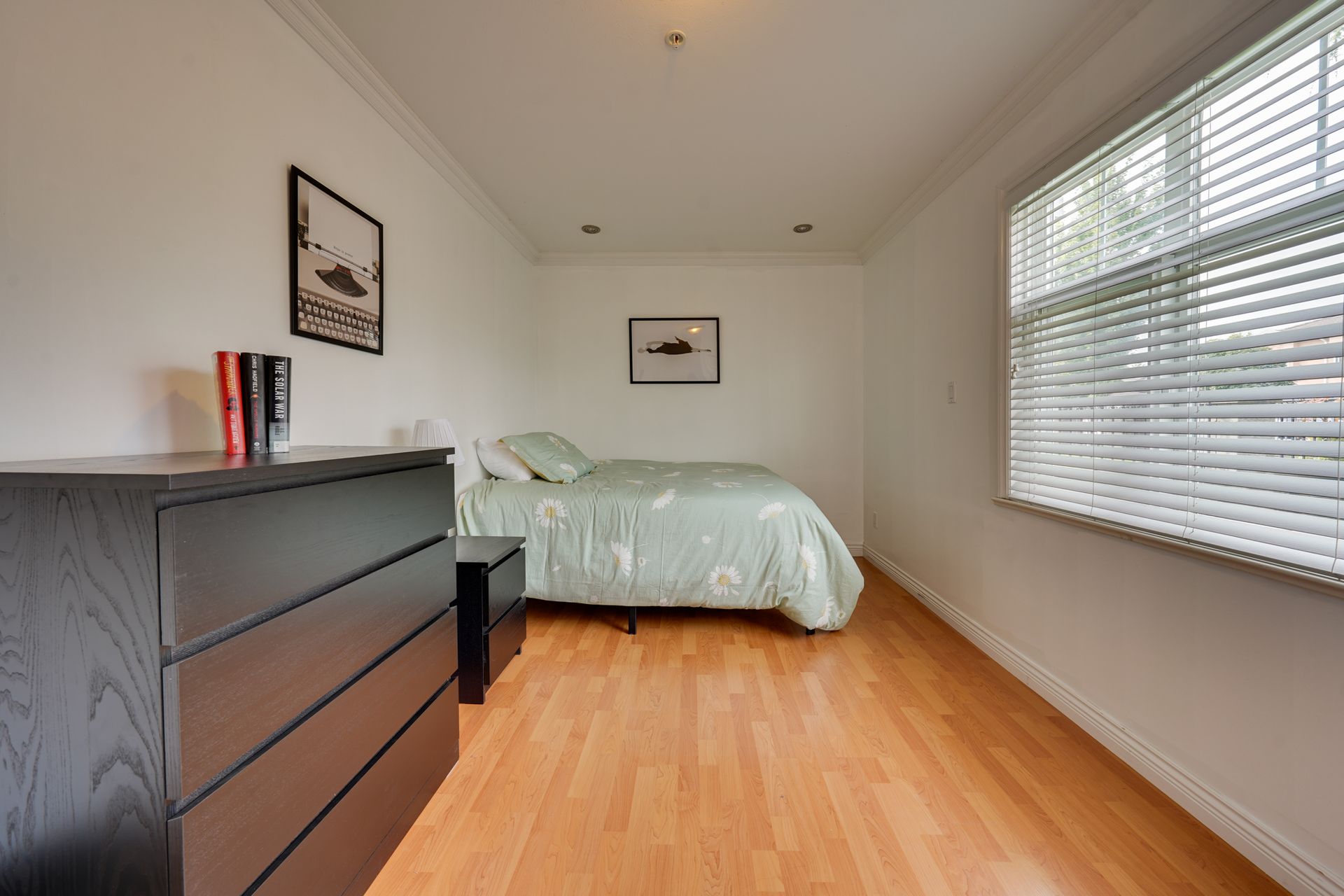 A bedroom with a bed , dresser , and window with blinds.